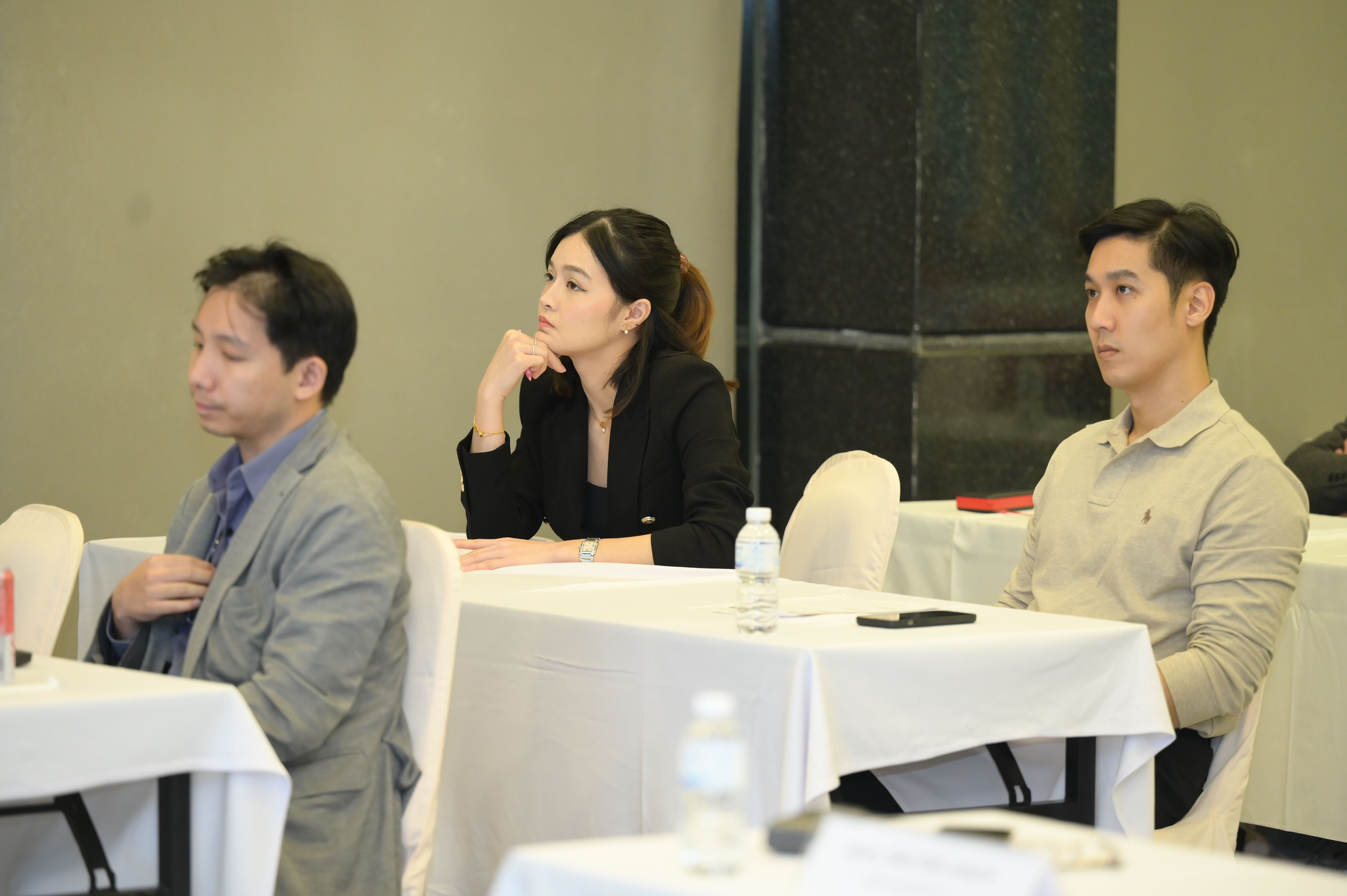 Three attendees listening attentively at a conference, two men and one woman.