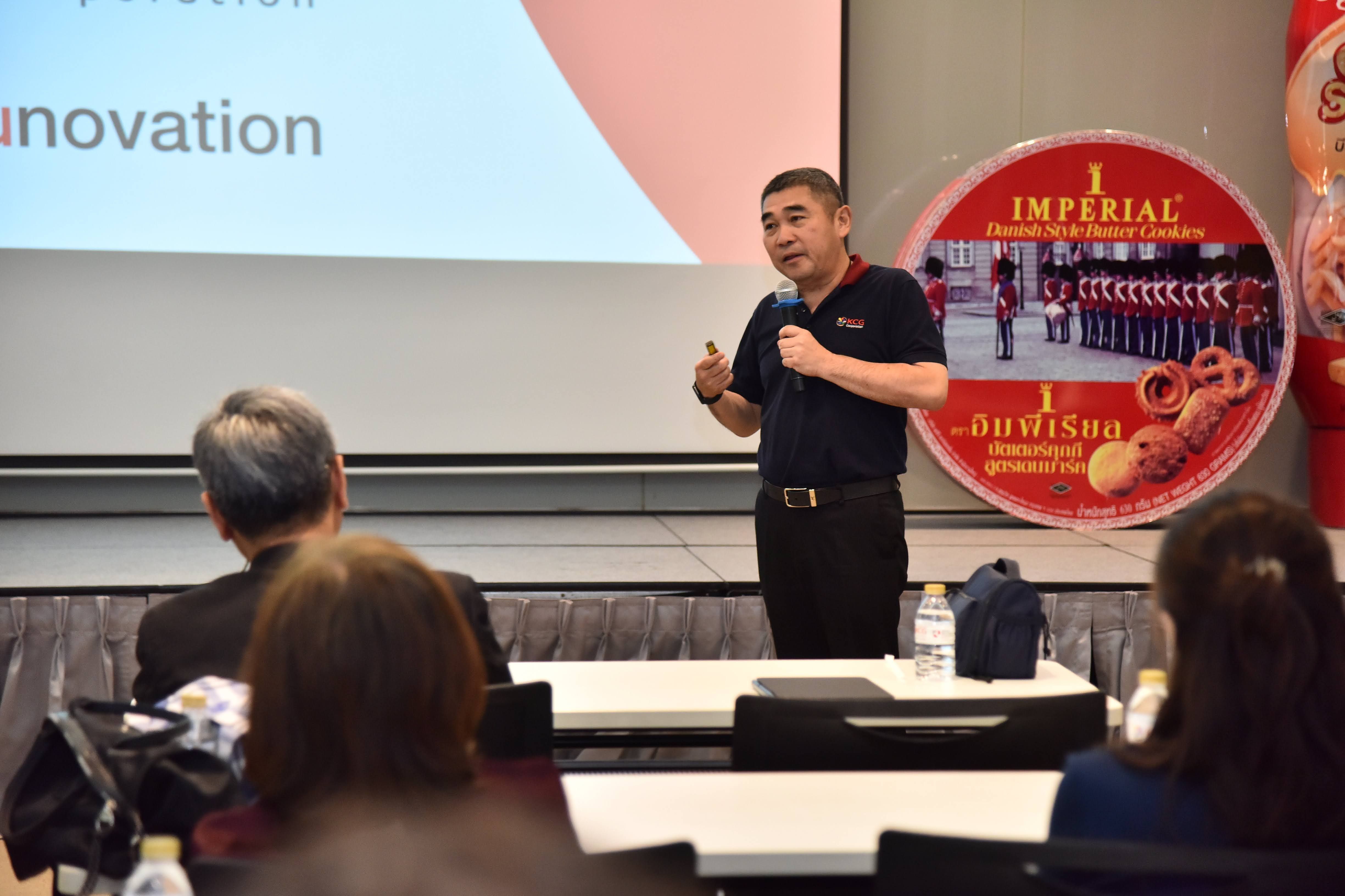Man presenting at a conference, gesturing to audience in front of Imperial sign.