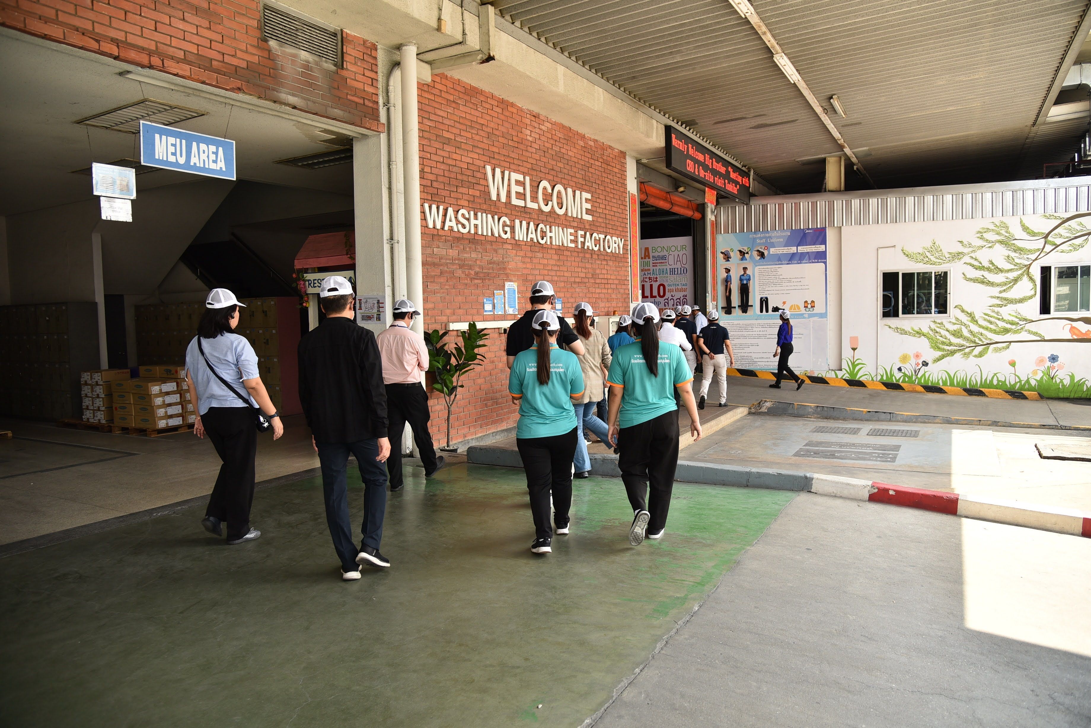 Group of people entering a building labeled 'WELCOME WASHING MACHINE FACTORY' for a tour.