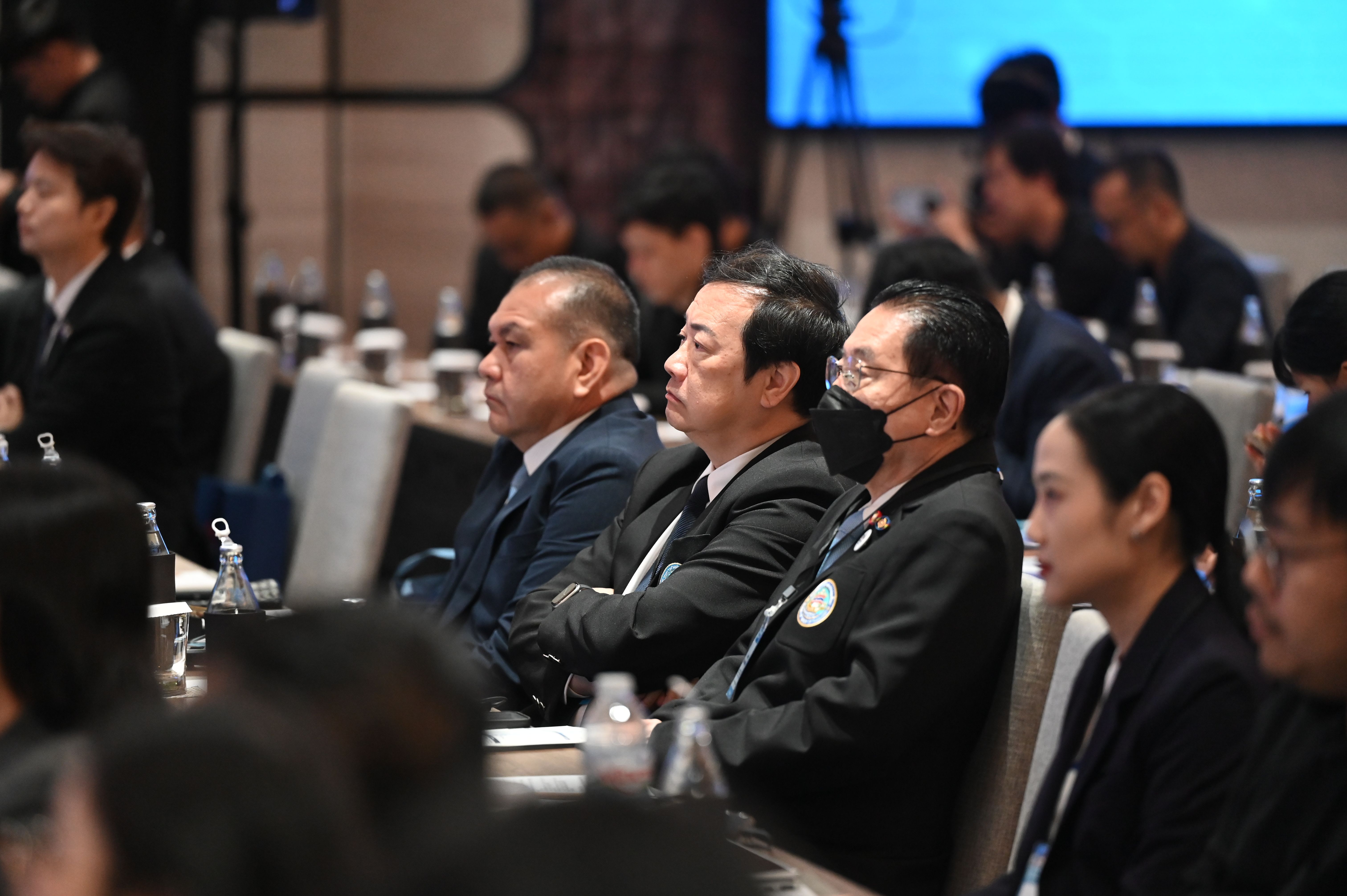 Conference attendees, including men in suits, listen attentively in a professional setting.