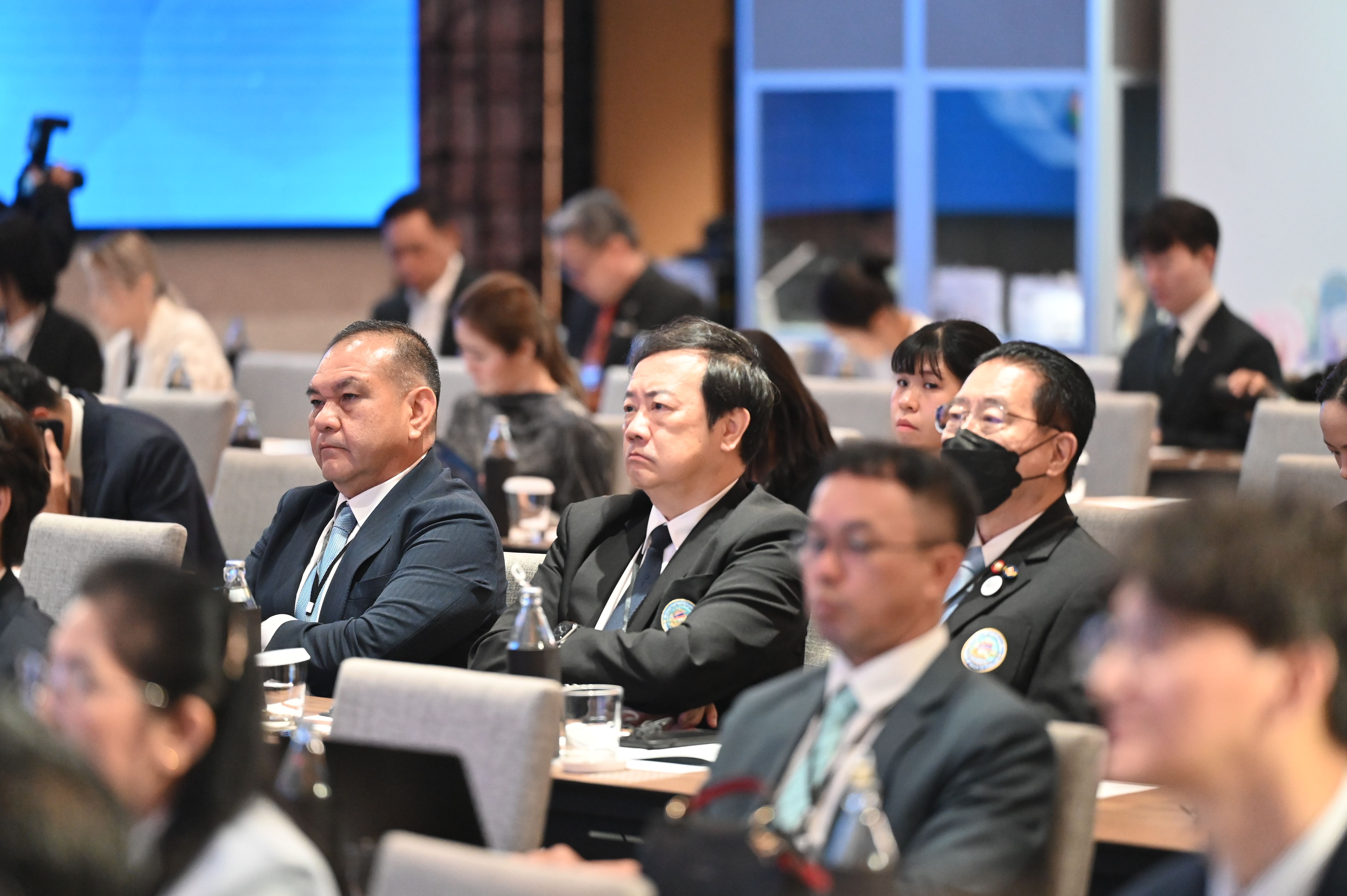 Men in suits attentively listen at a formal conference or meeting event.