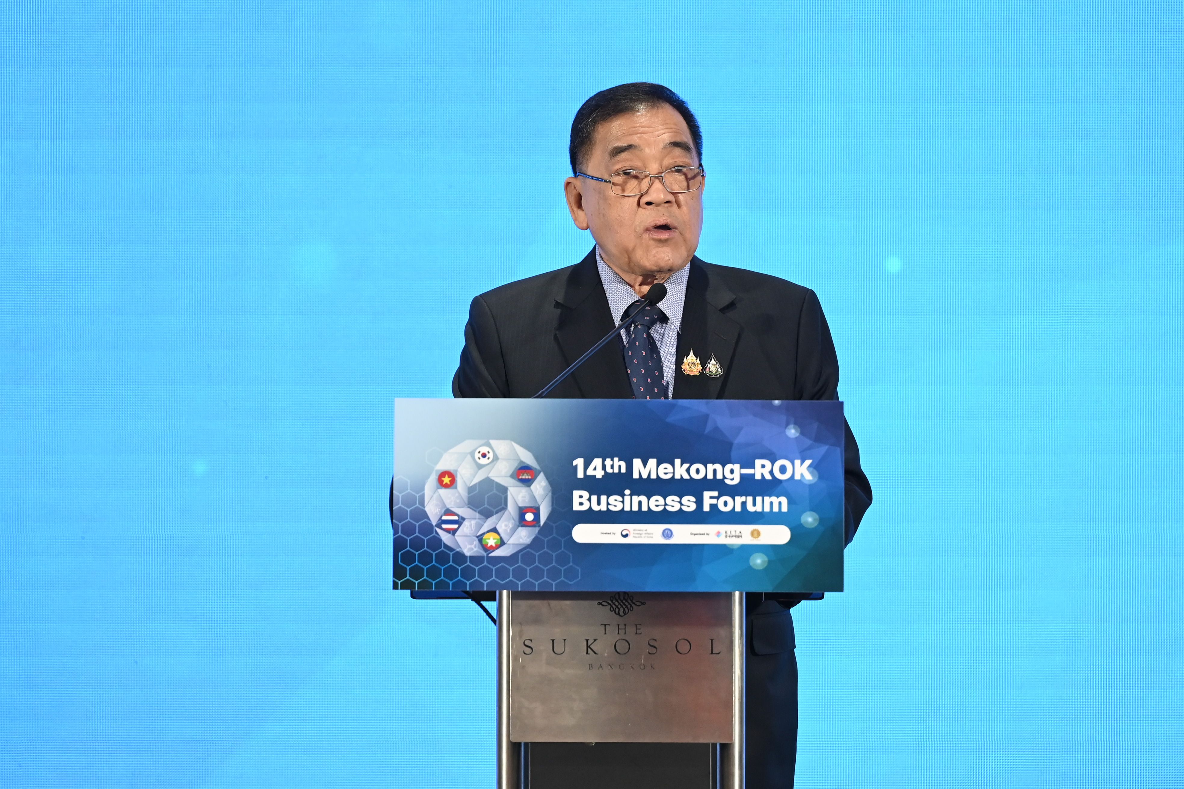 A man in a dark suit speaks at a podium with '14th Mekong-ROK Business Forum' text.