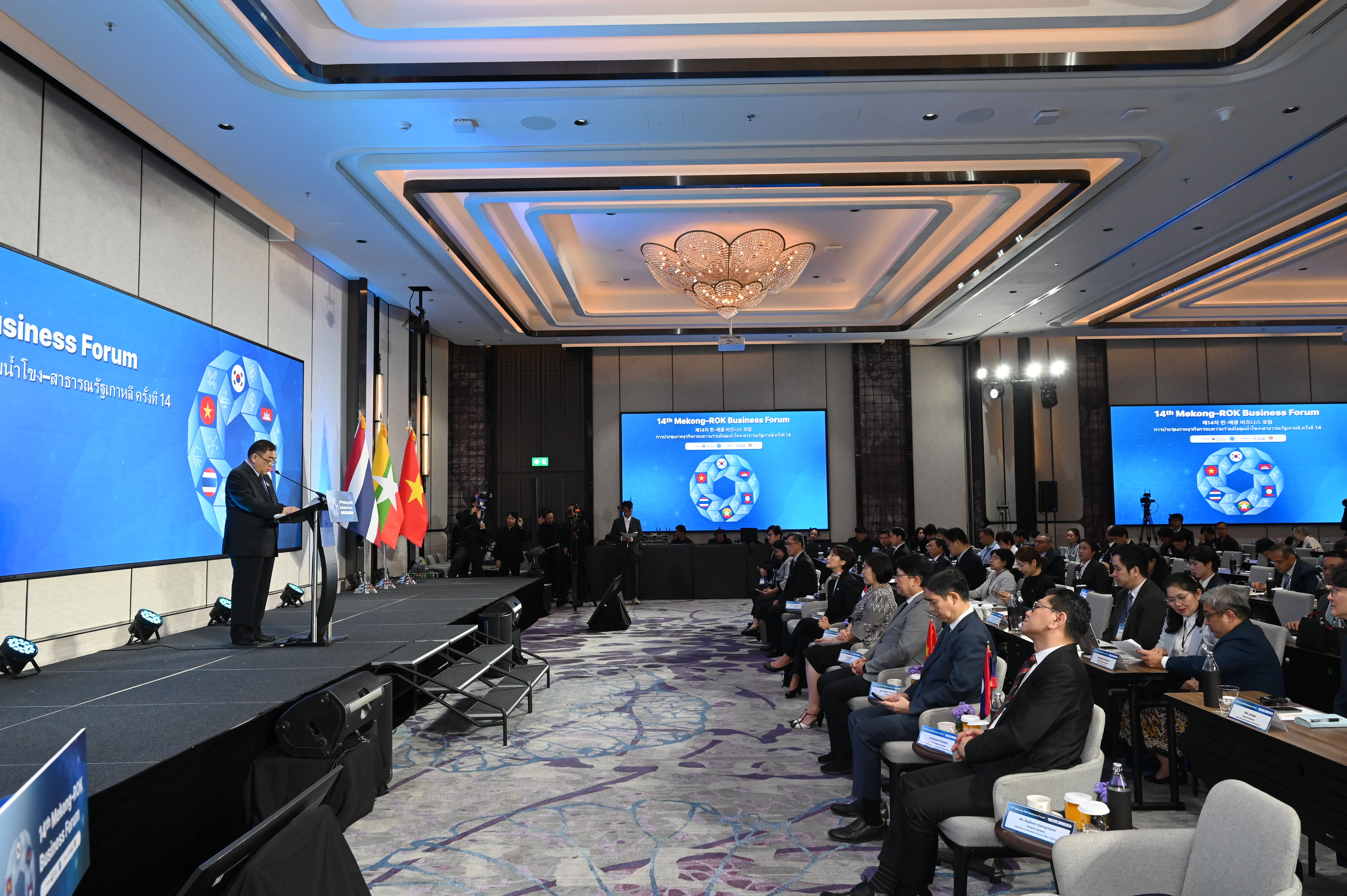 Man in suit speaks at podium on stage during a business forum event.