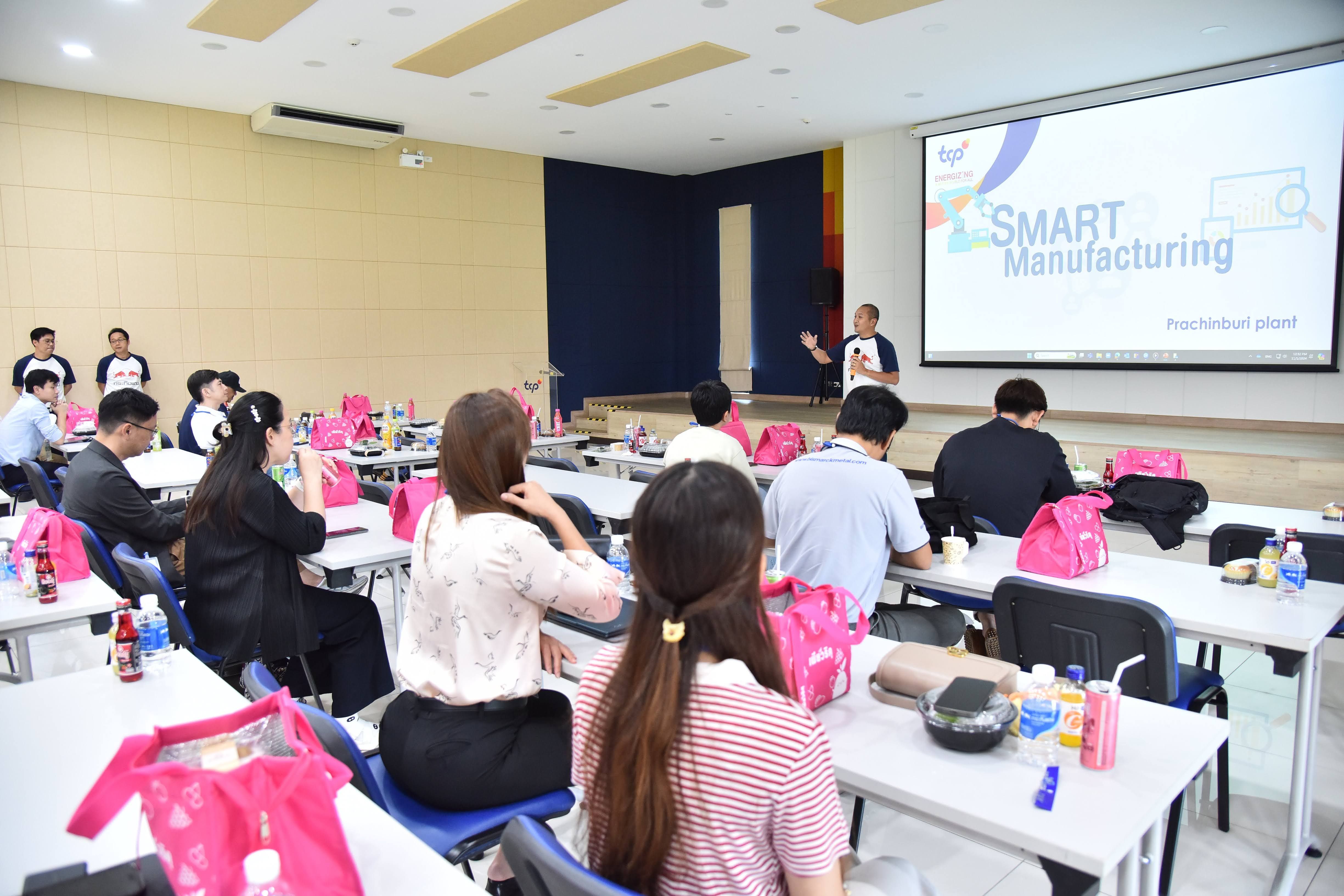 Attendees watch a presenter next to a screen displaying 'SMART Manufacturing' in a seminar room.