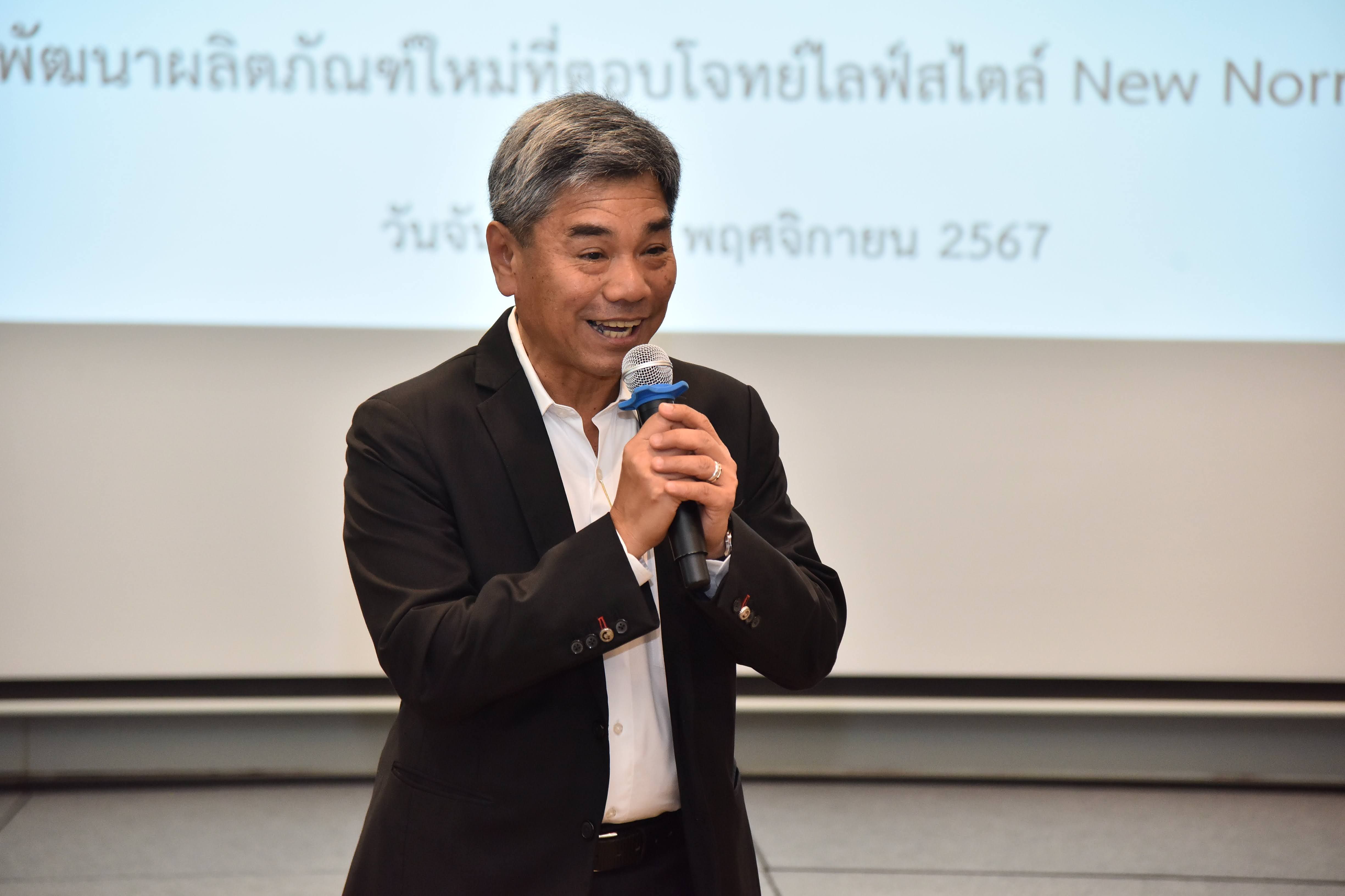 A smiling man in a suit jacket speaks into a microphone during a presentation.