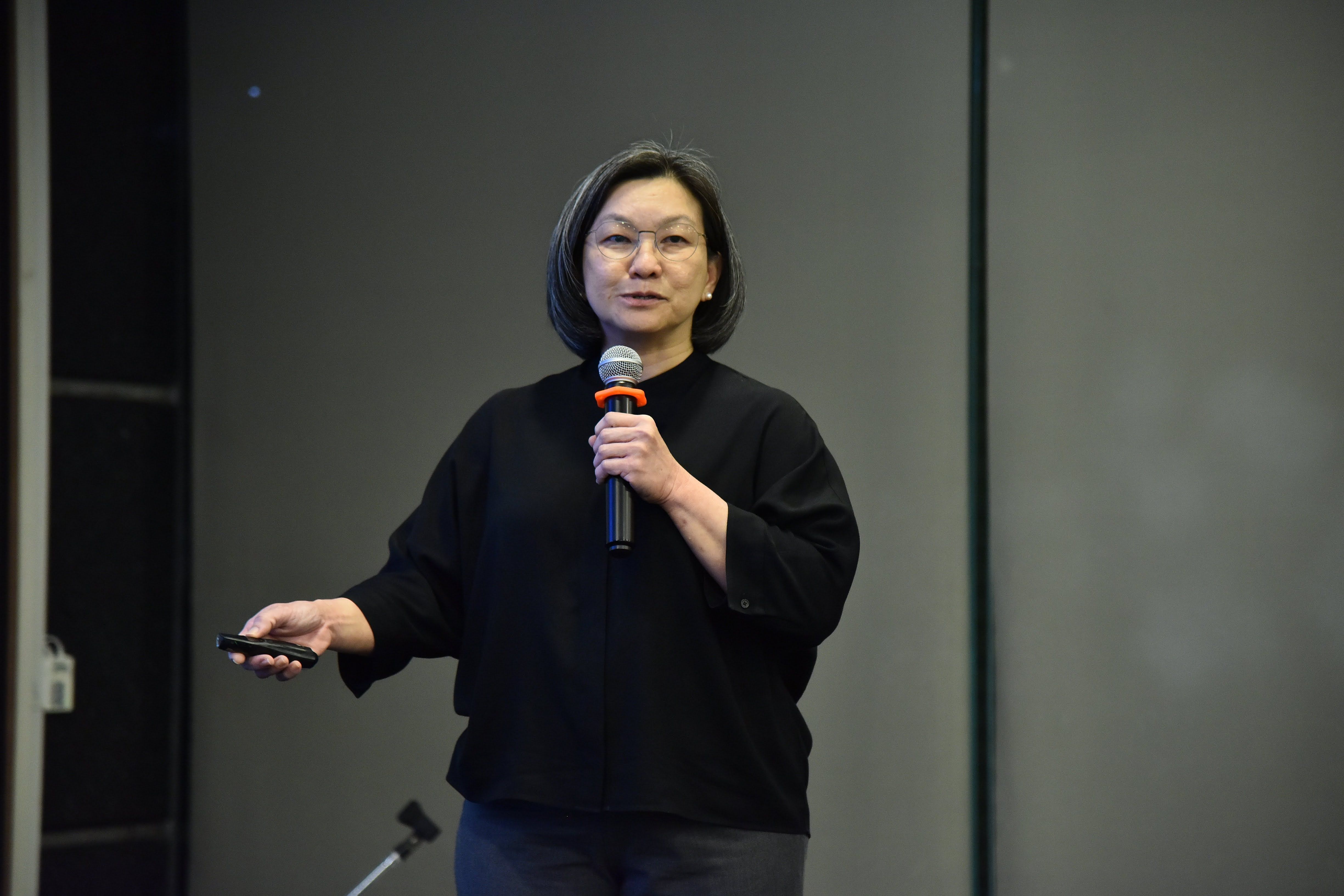 Woman presenting, speaking into a microphone while holding a remote clicker.