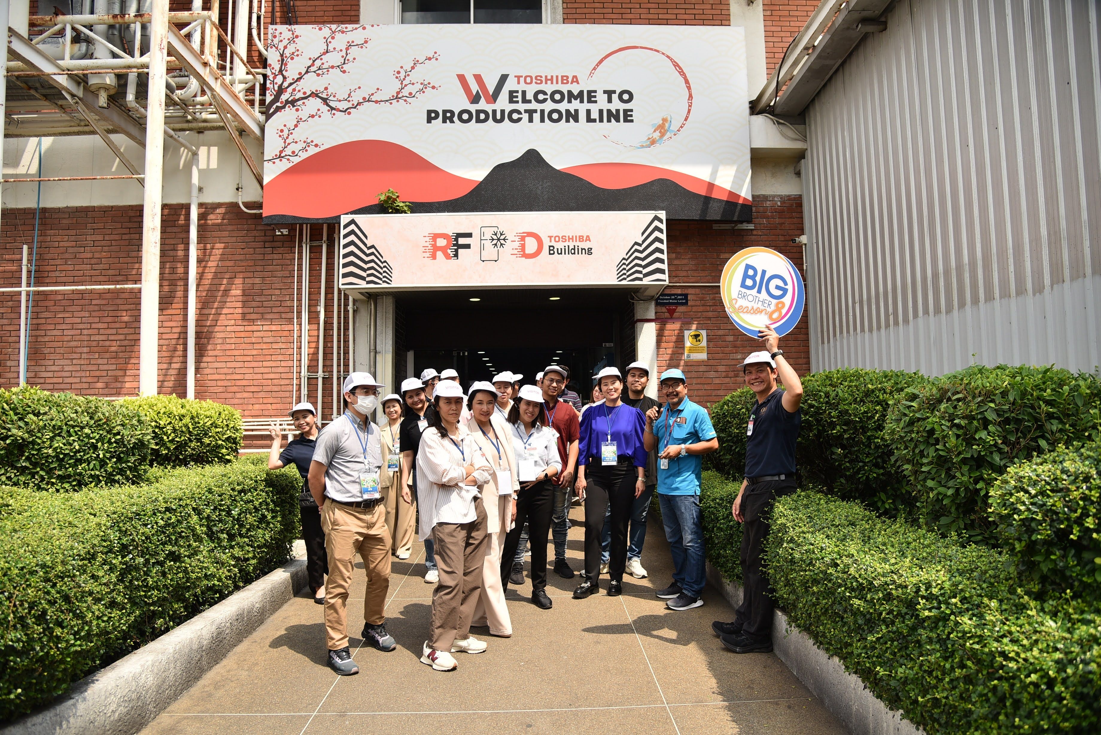 Group of visitors stand outside AJE factory entrance with a 'Welcome to Production Line' sign.