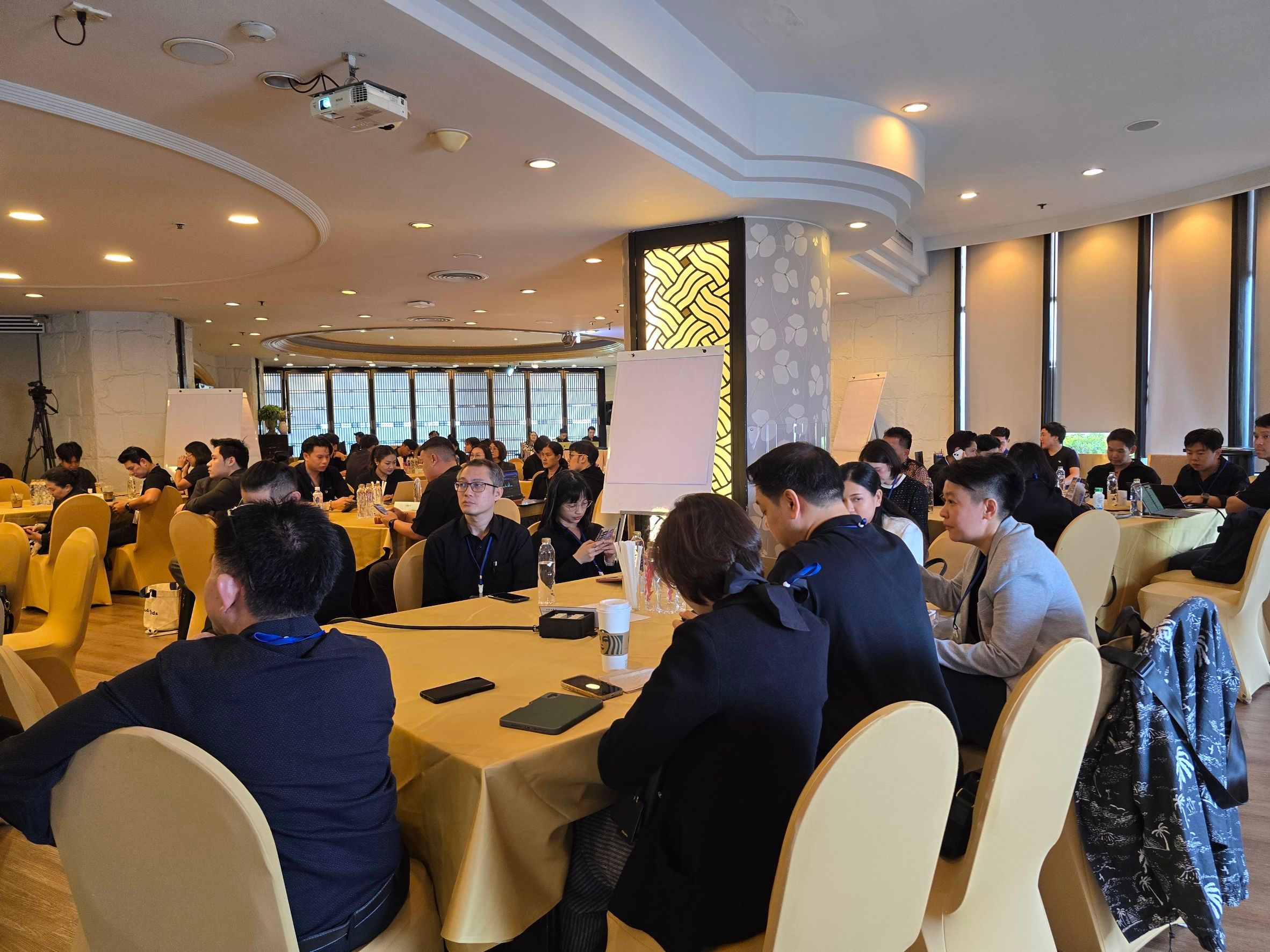 Conference attendees gather around tables in a brightly lit meeting room.