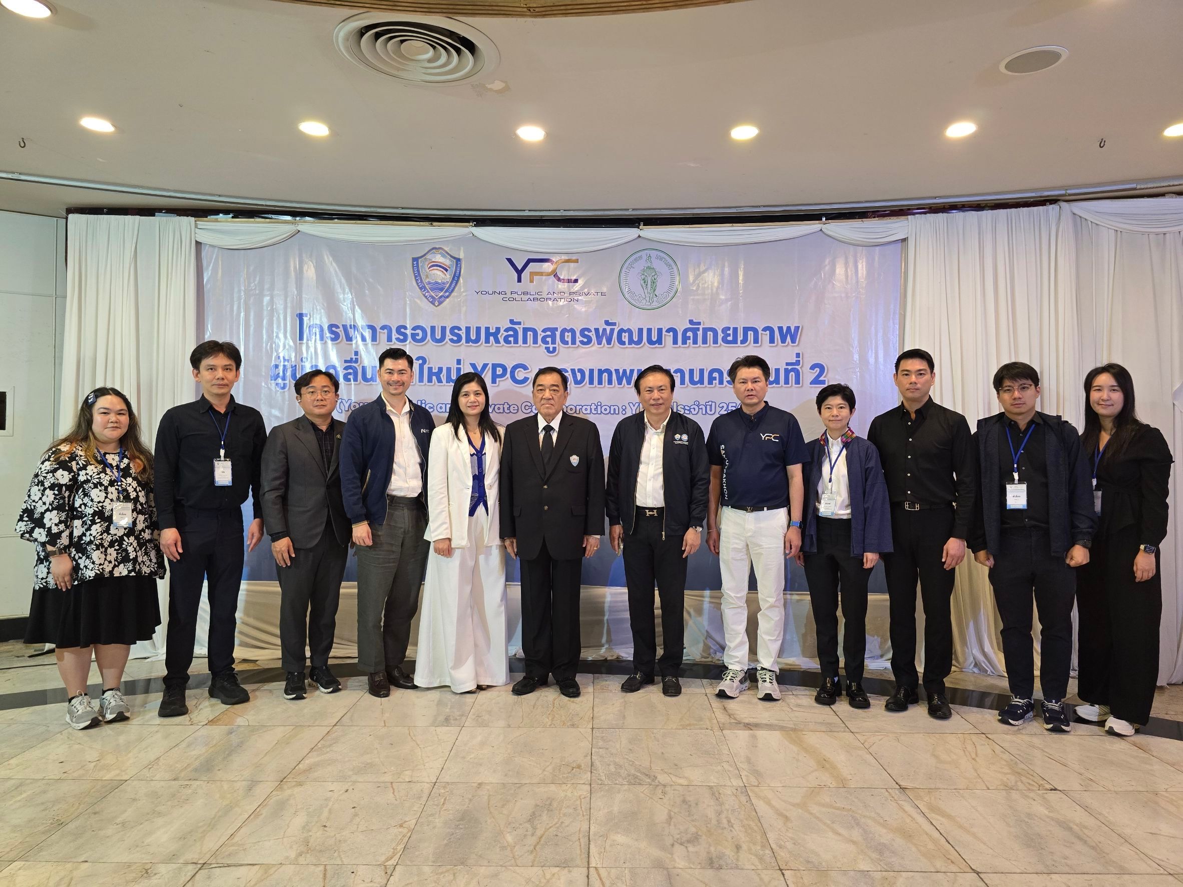 A group of professionals in formal attire stands before a banner at an indoor event.