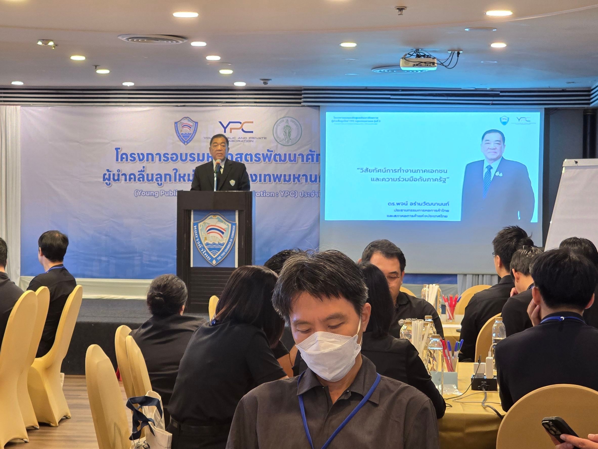 A man speaks at a podium during a conference with an audience present.