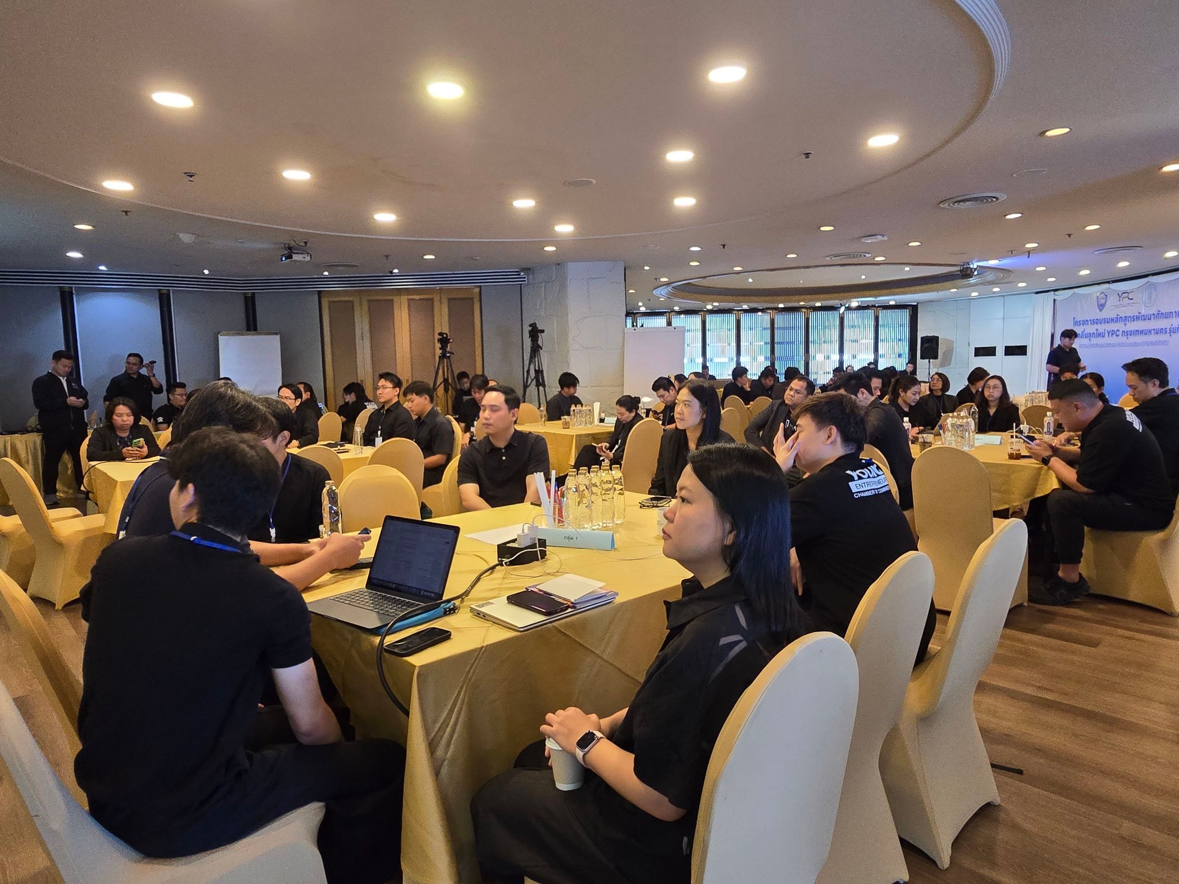 Attendees engage in discussions around yellow-draped tables in a bright conference room setting.