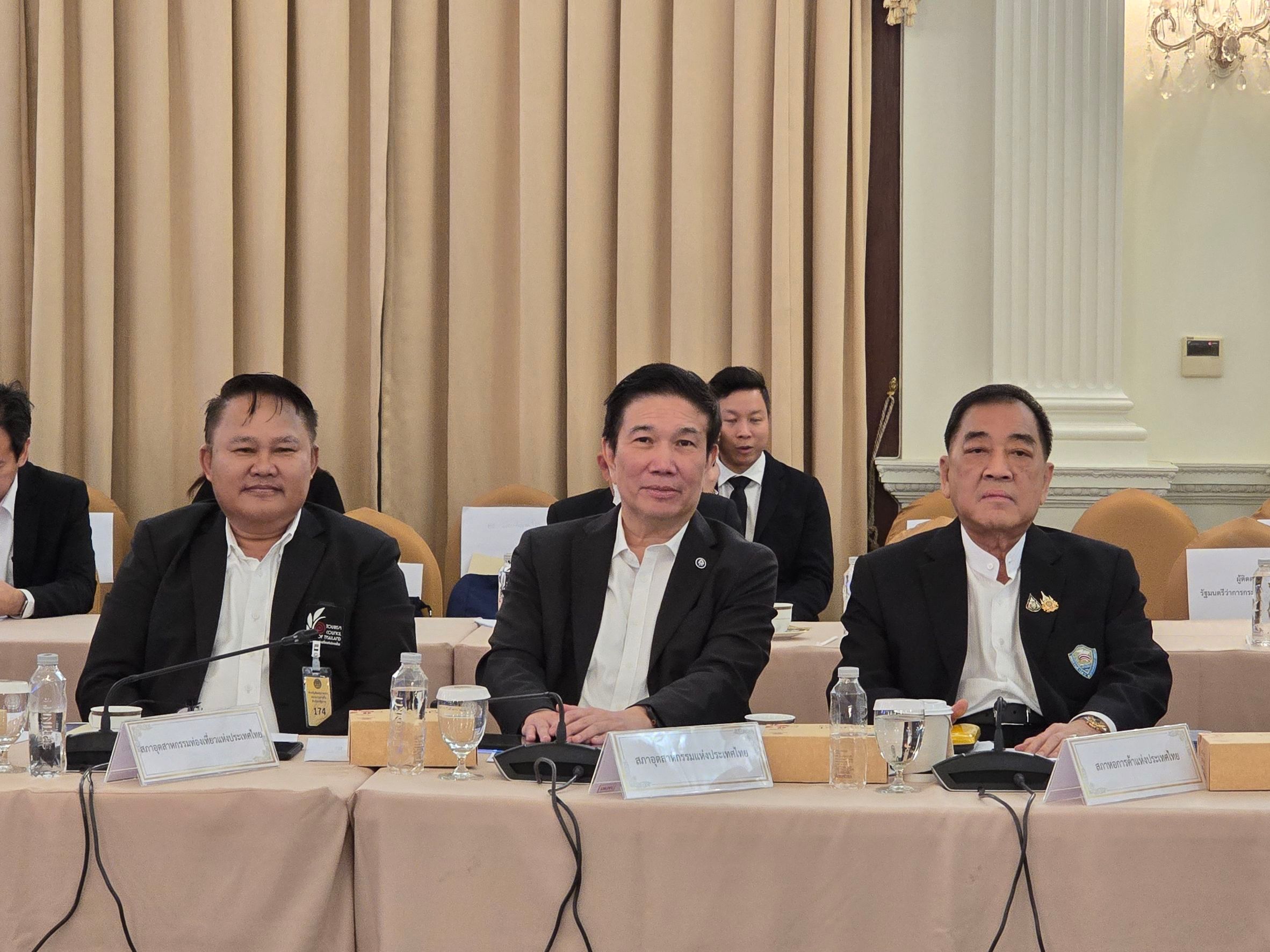 Three men in black suits sit smiling at a long table during a meeting.