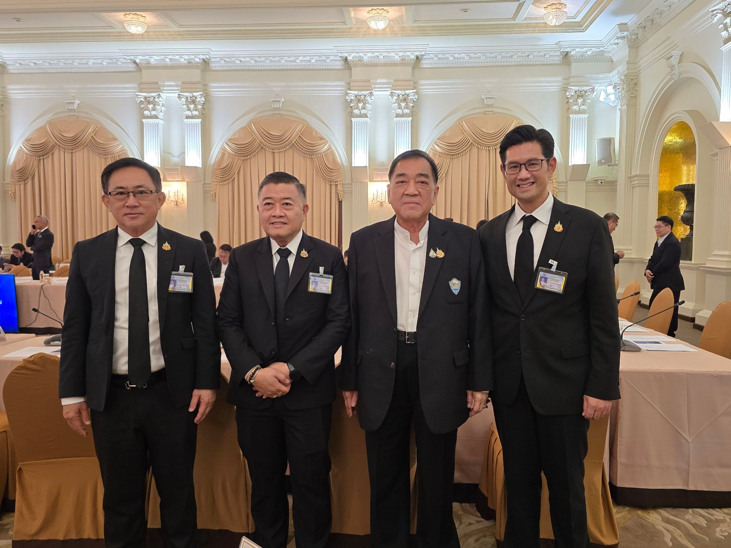 Four men in dark suits standing together at a formal conference event.