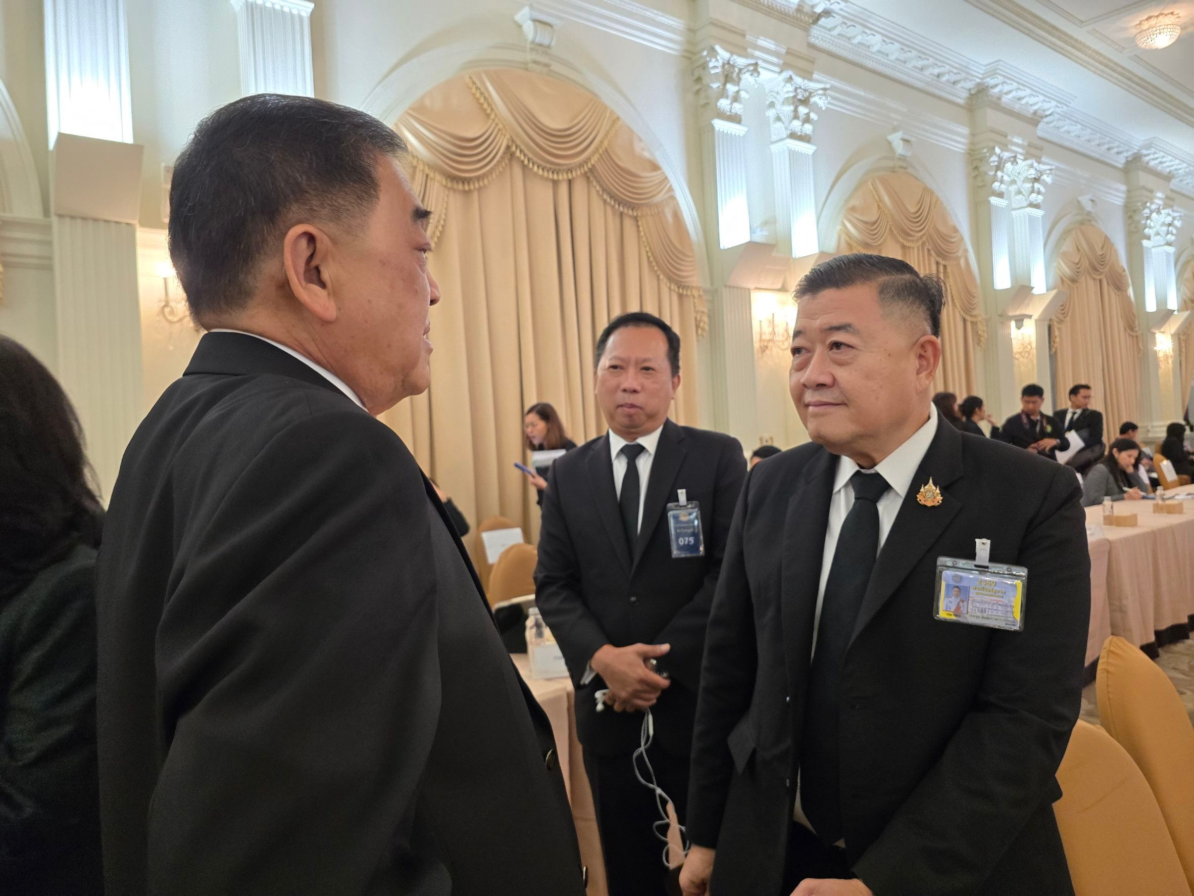 Three men in black suits conversing in a formal event hall.