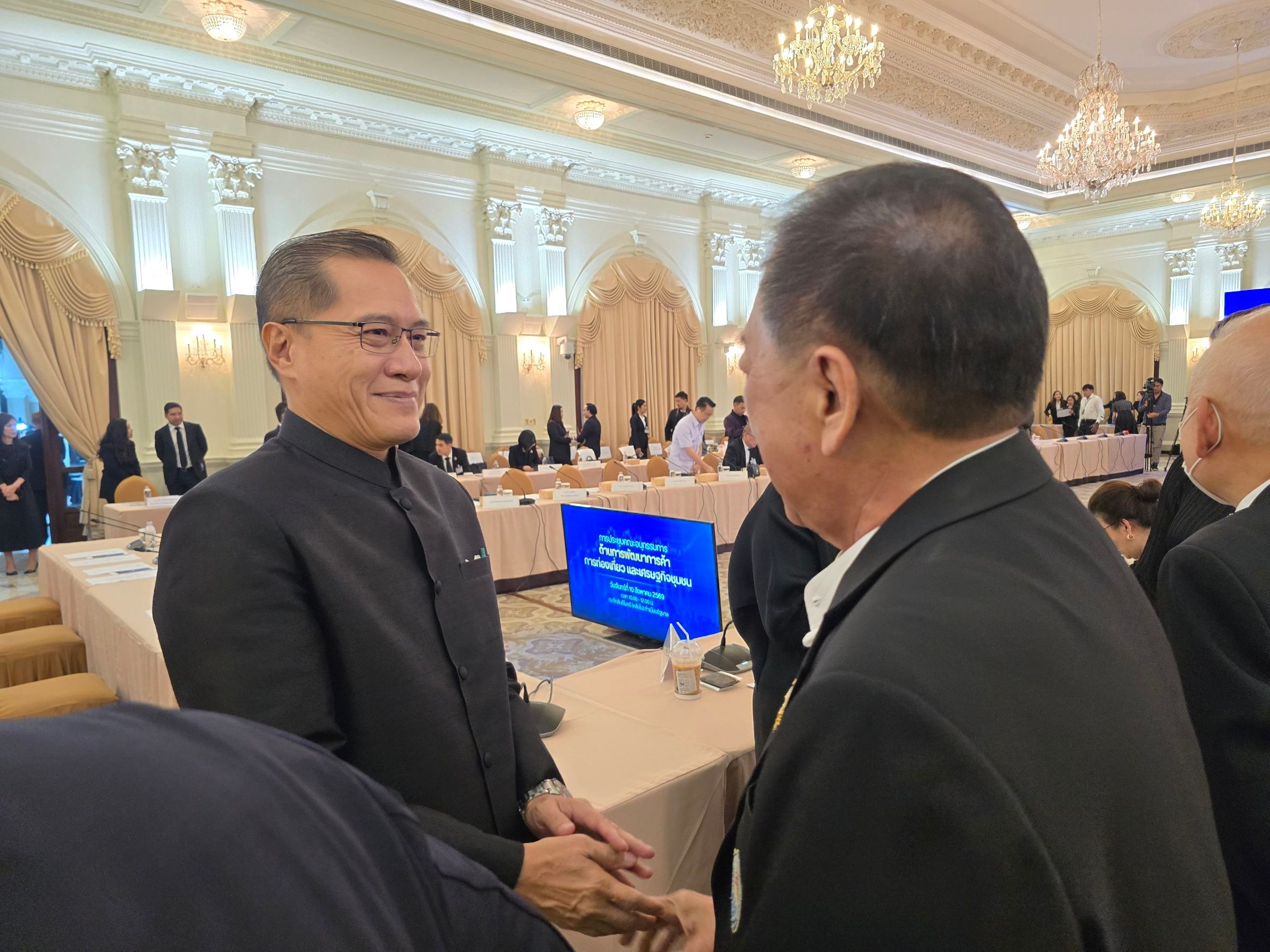 Two men in suits greet each other at a formal event, smiling warmly.
