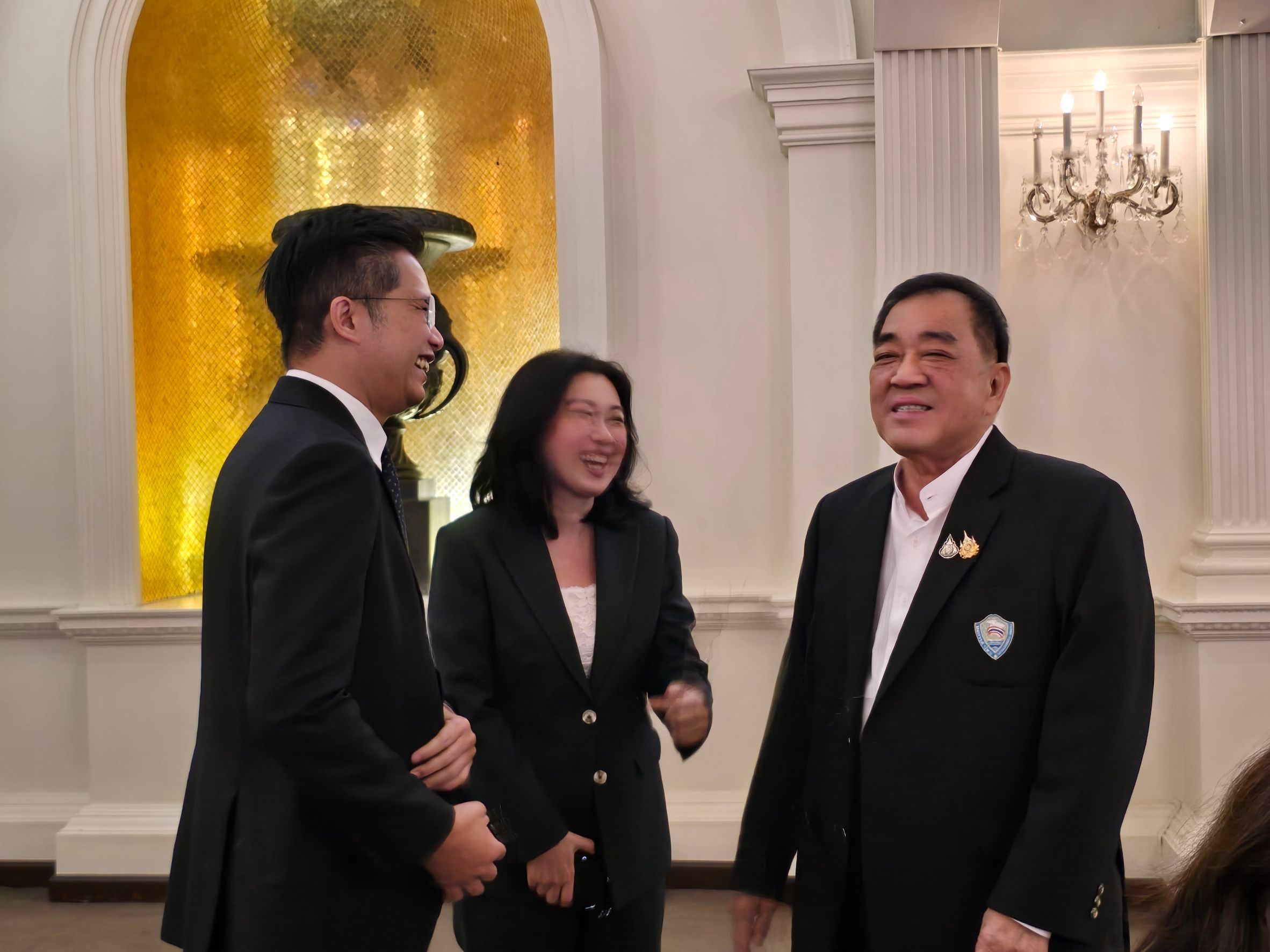 Three formally dressed professionals converse and laugh at an indoor event.