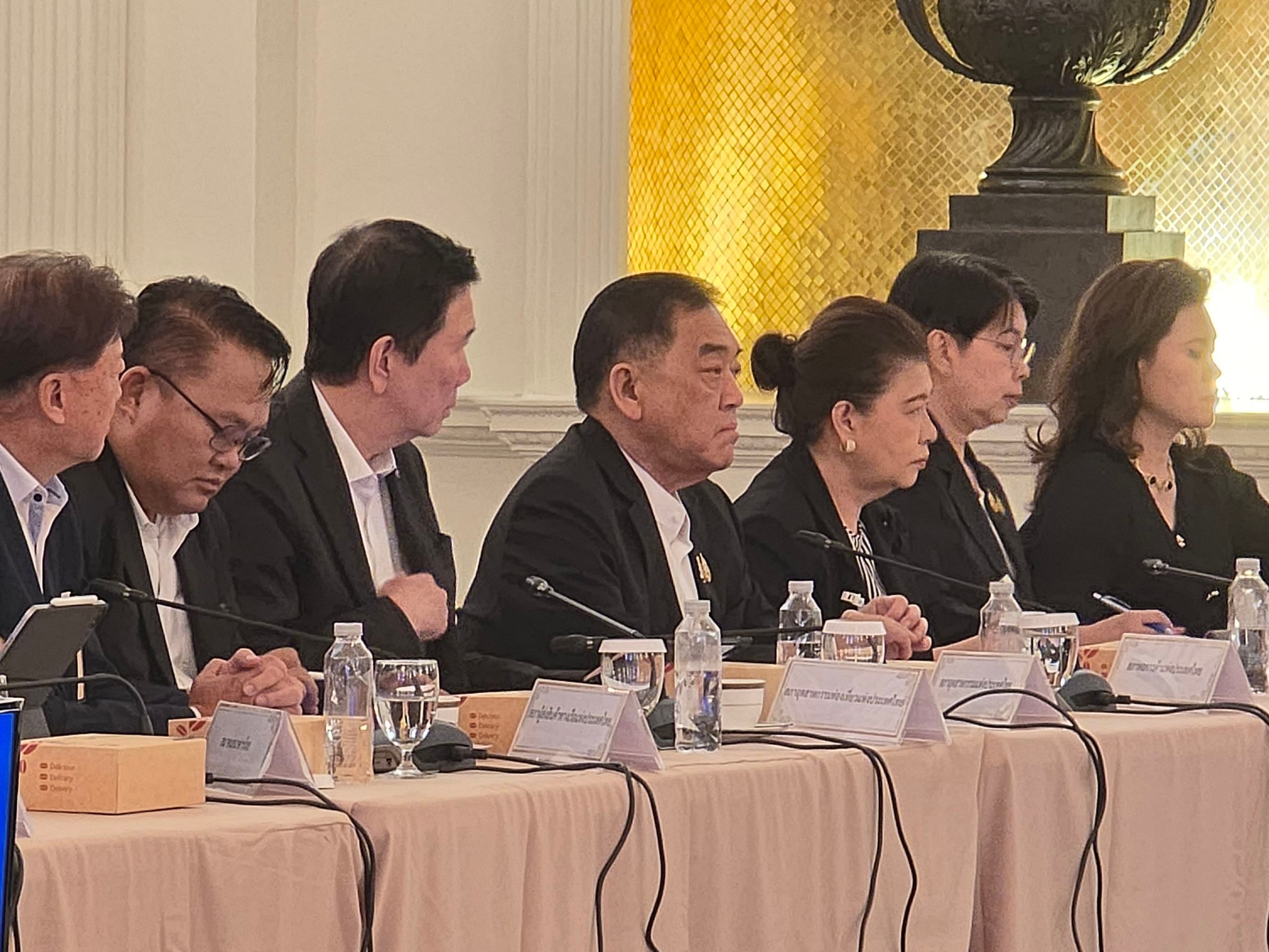 A group of formally dressed individuals attends a meeting at a long conference table.
