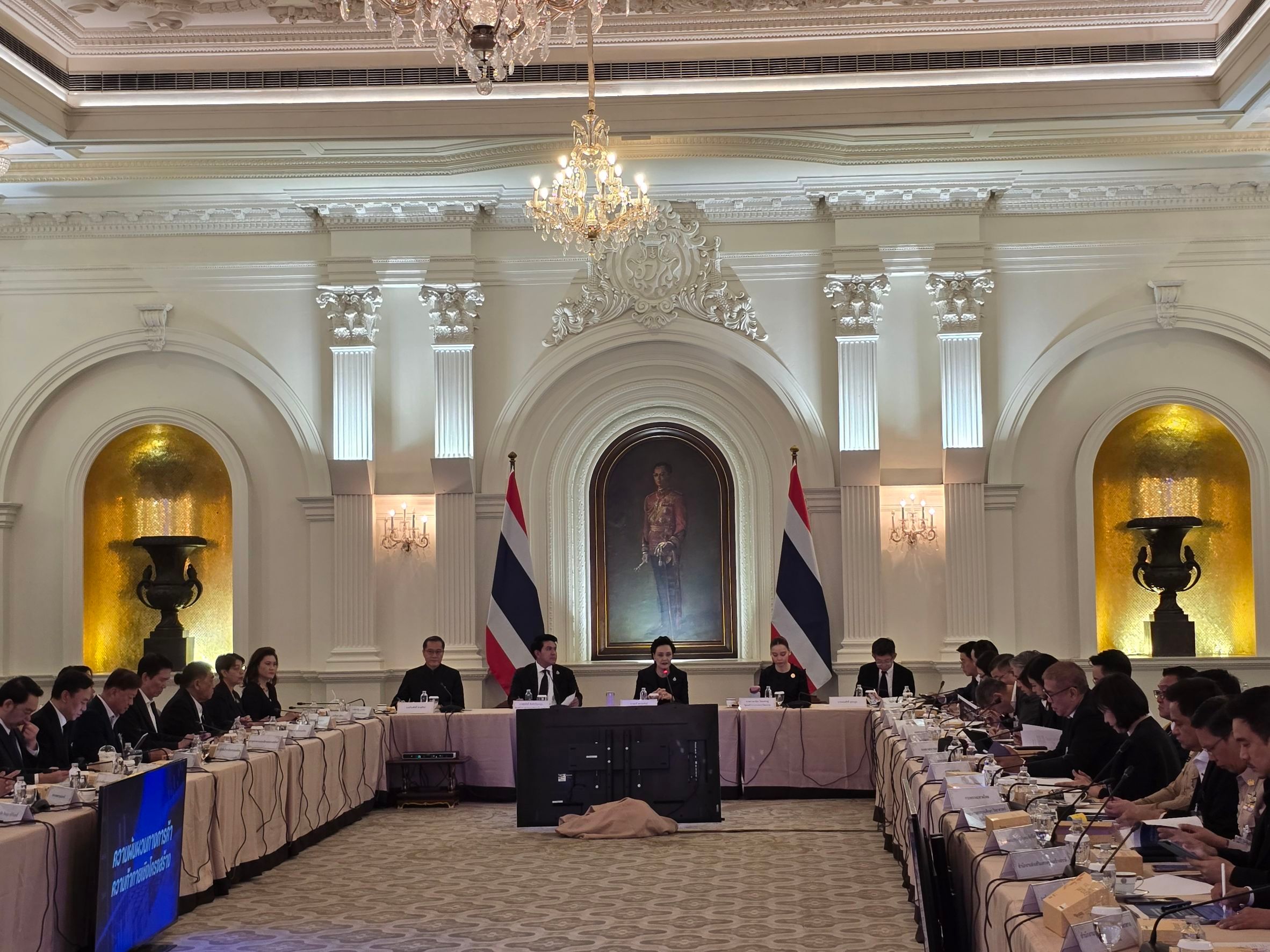 Formal meeting room with attendees seated at U-shaped tables under Thai flags.