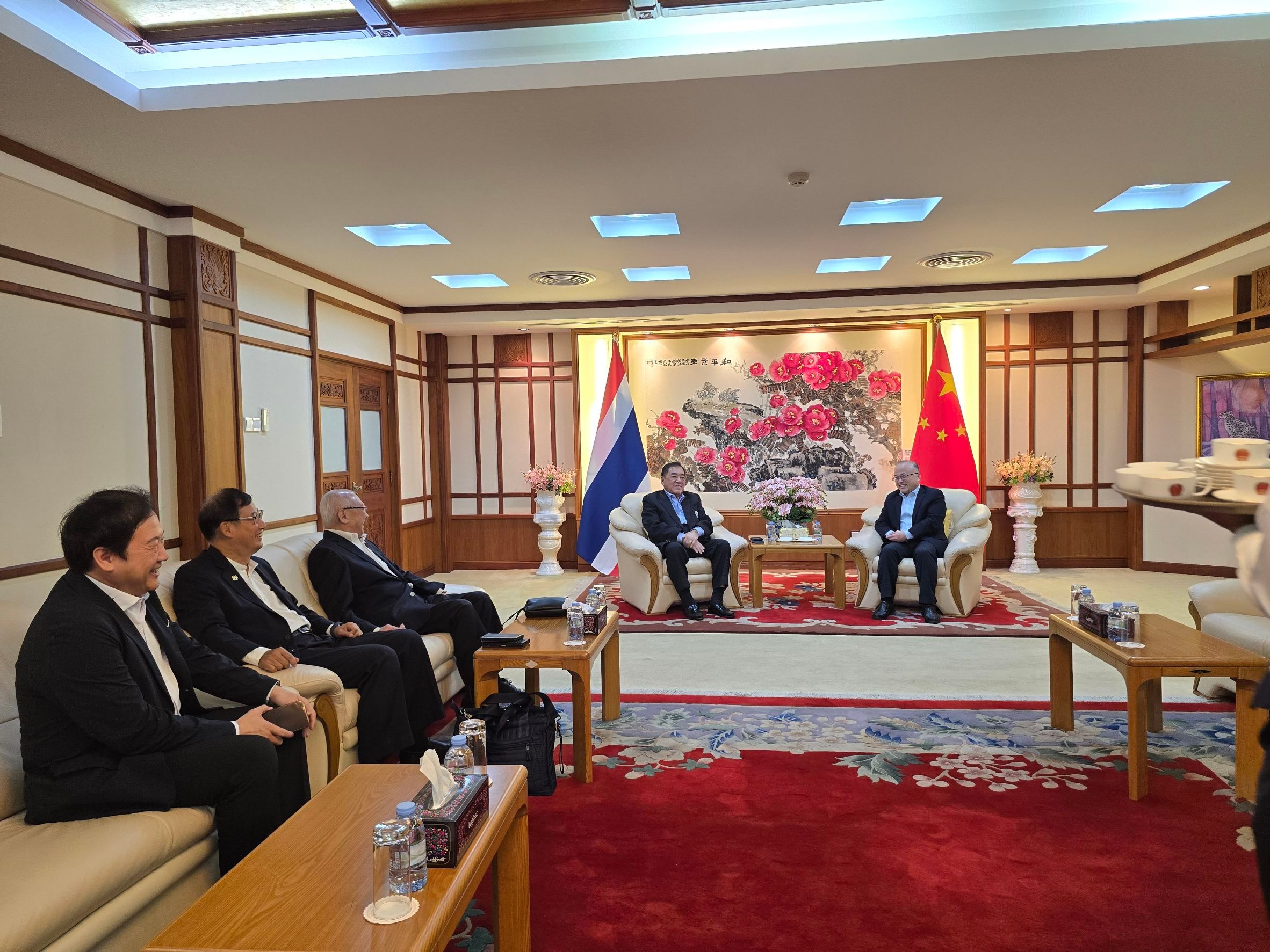 Two delegates discuss diplomacy in a formal meeting room with Thai and Chinese flags.