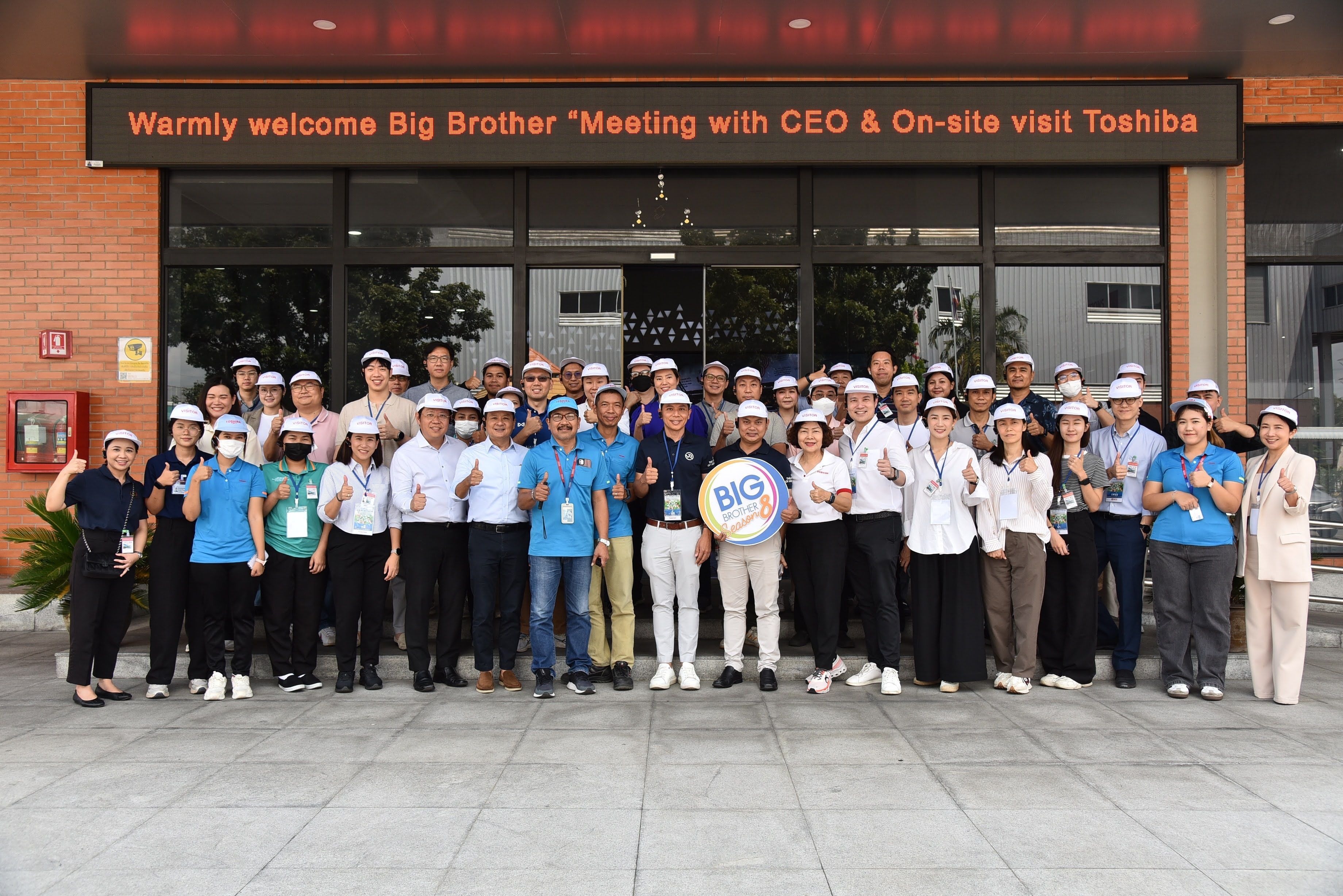 A large group of employees and visitors pose in front of the Toshiba building.
