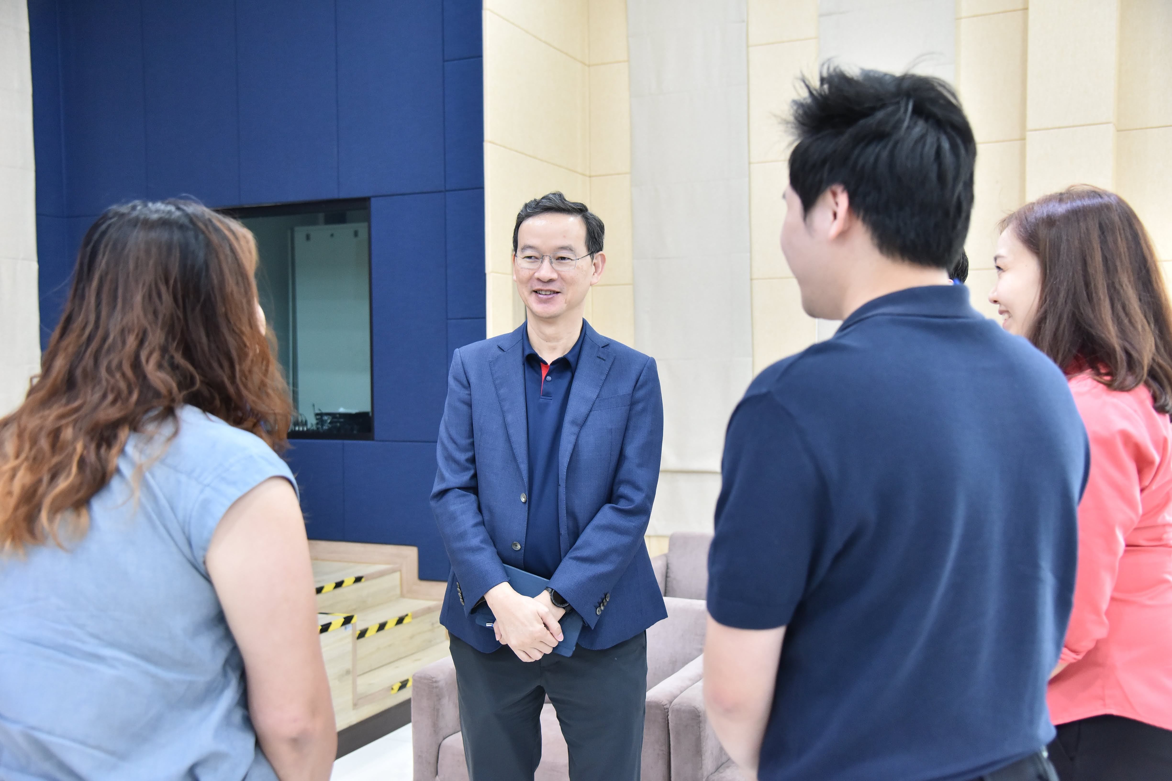 Man in blue suit smiling at three people in a modern indoor setting.