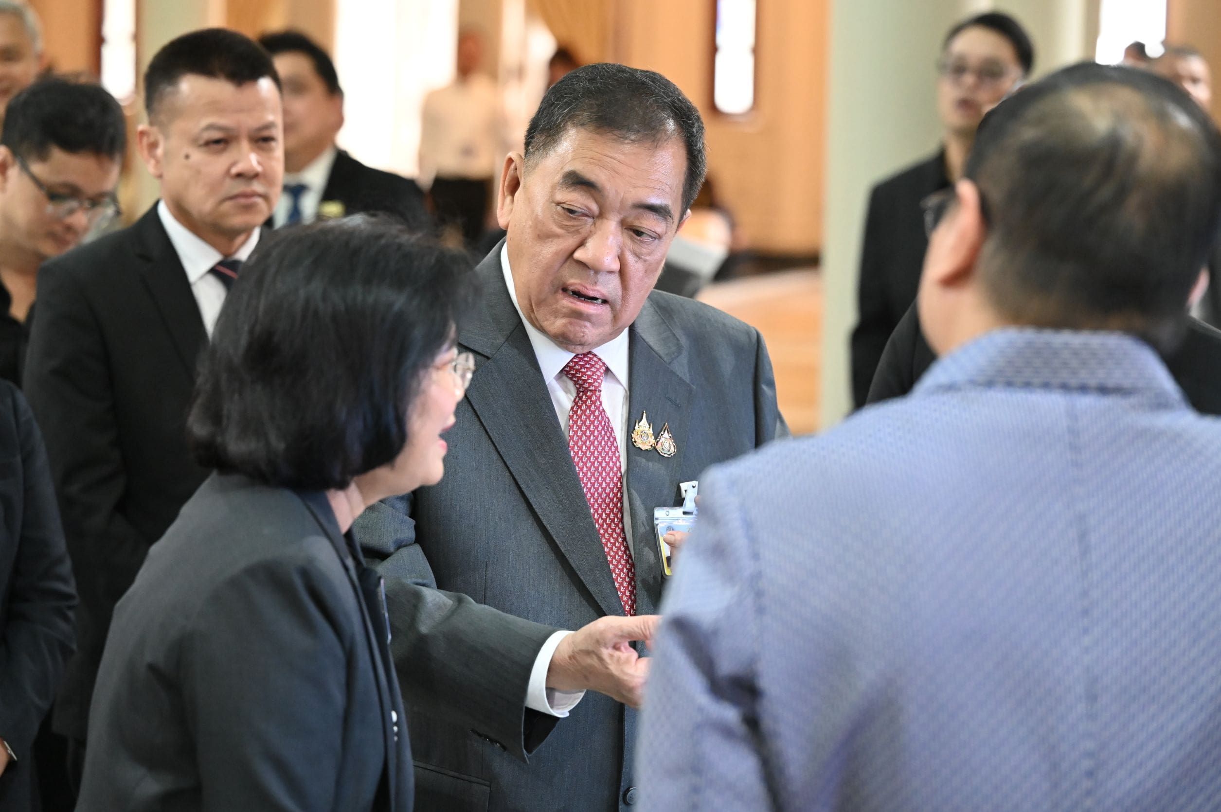 Man in dark suit and medals speaks to woman at a formal indoor event.