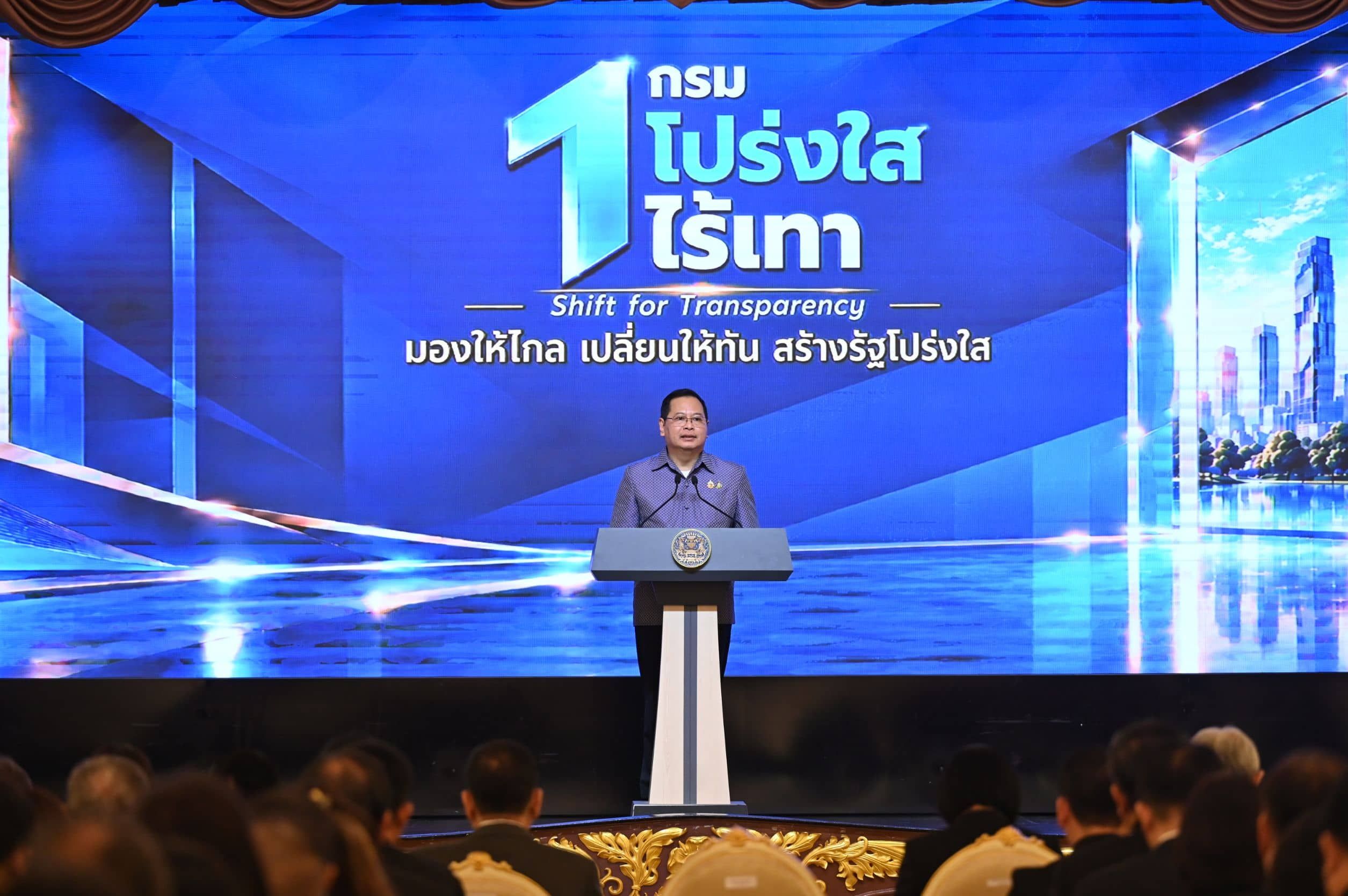 Man speaks at a podium before a large screen displaying 'Shift for Transparency' and Thai text.