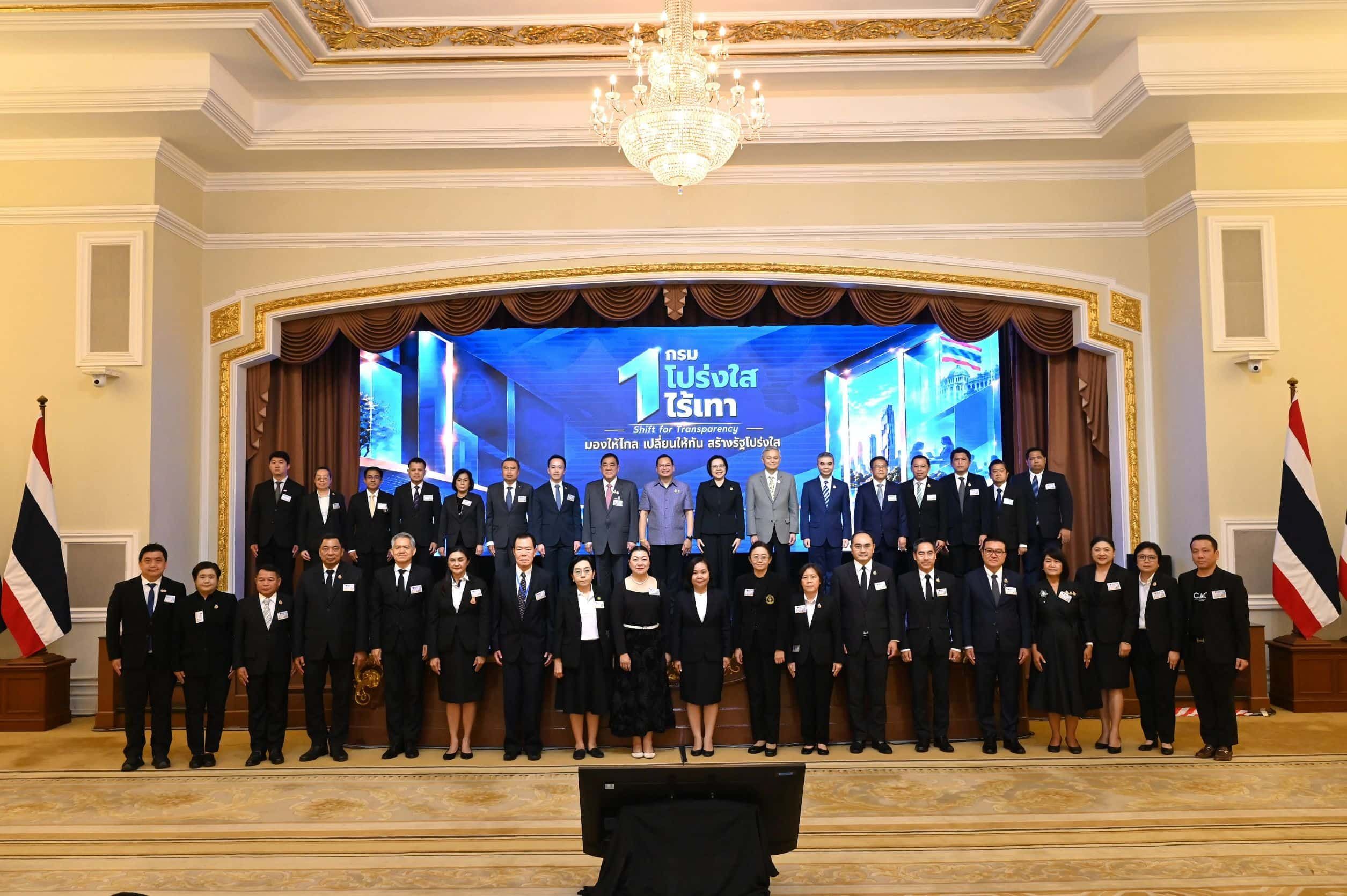 Large group of formally dressed people stand for a photo in an ornate official hall.