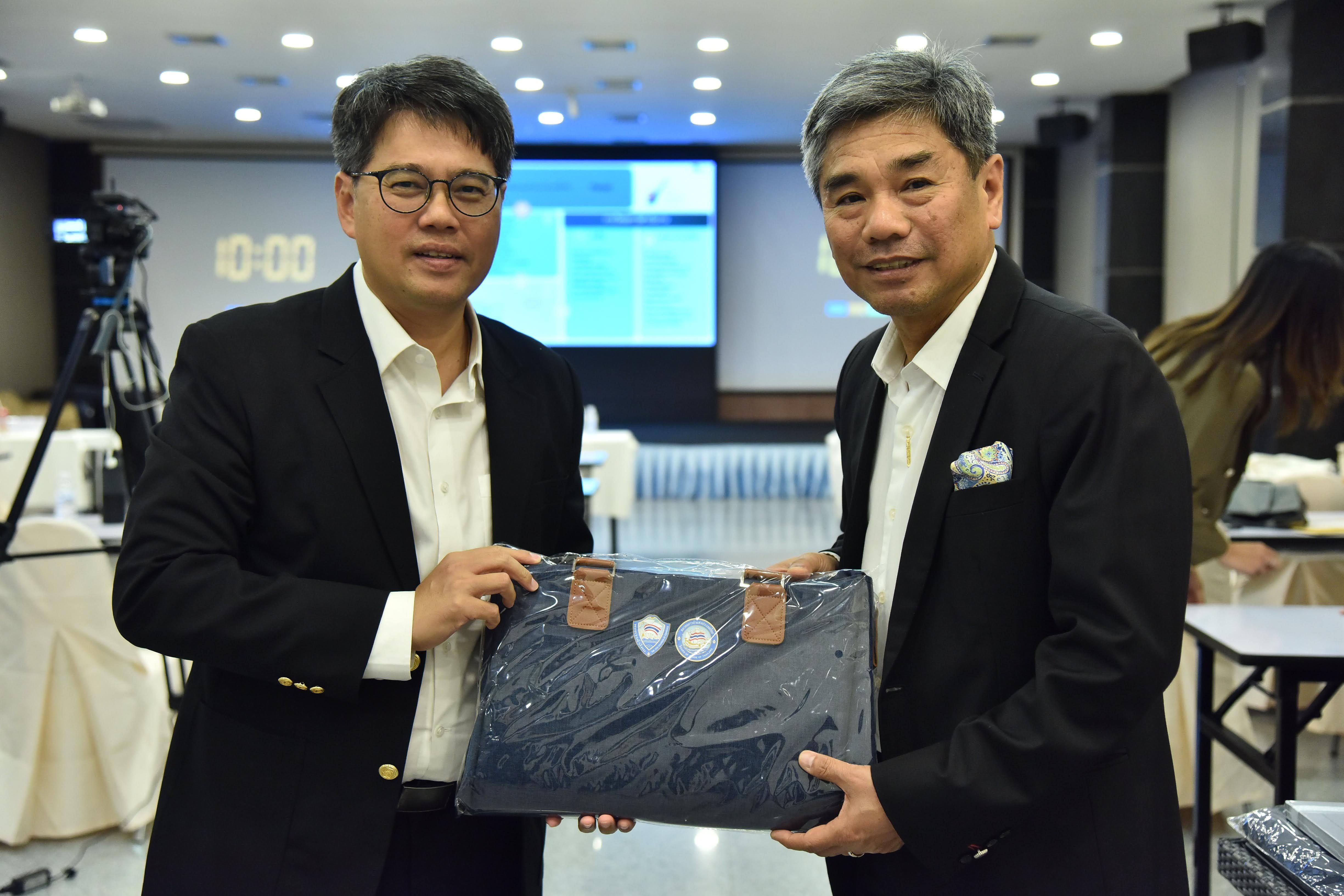 Two executives in suits exchange a blue wrapped gift package in a meeting room.