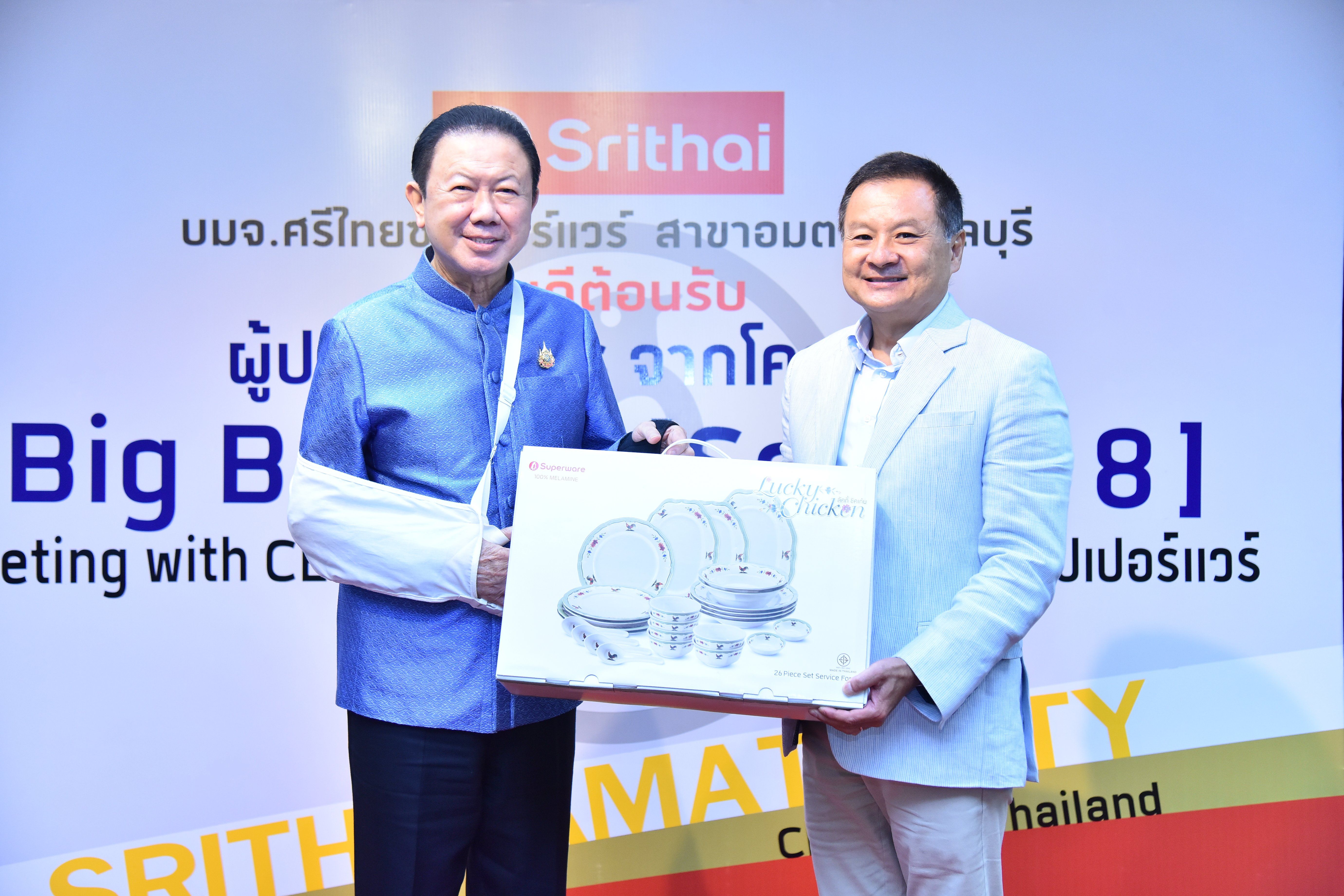 Two executives, one with an arm sling, exchange a framed gift at a corporate event.