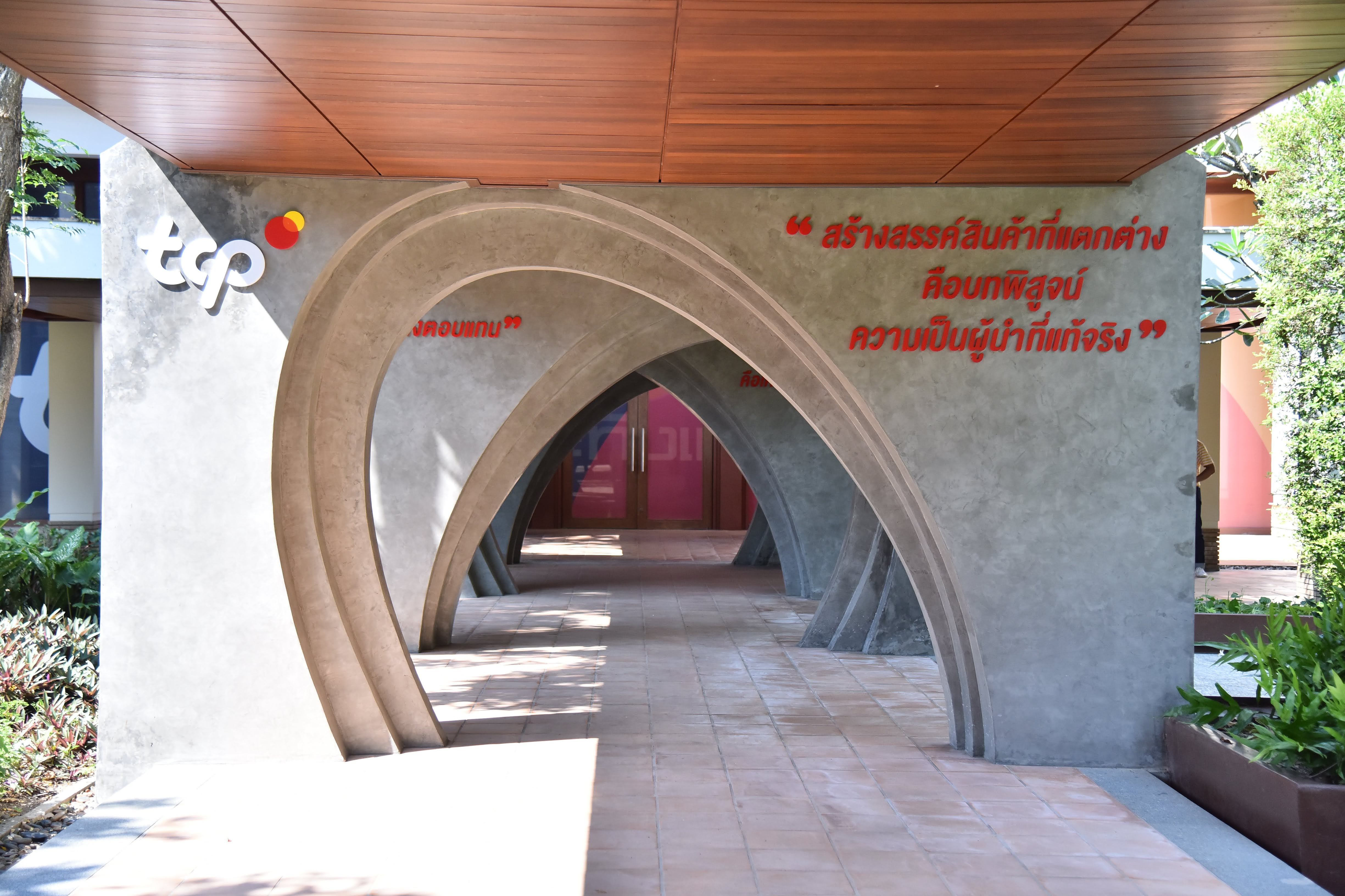 Modern concrete archway entrance with a wooden ceiling and Thai script on the wall.