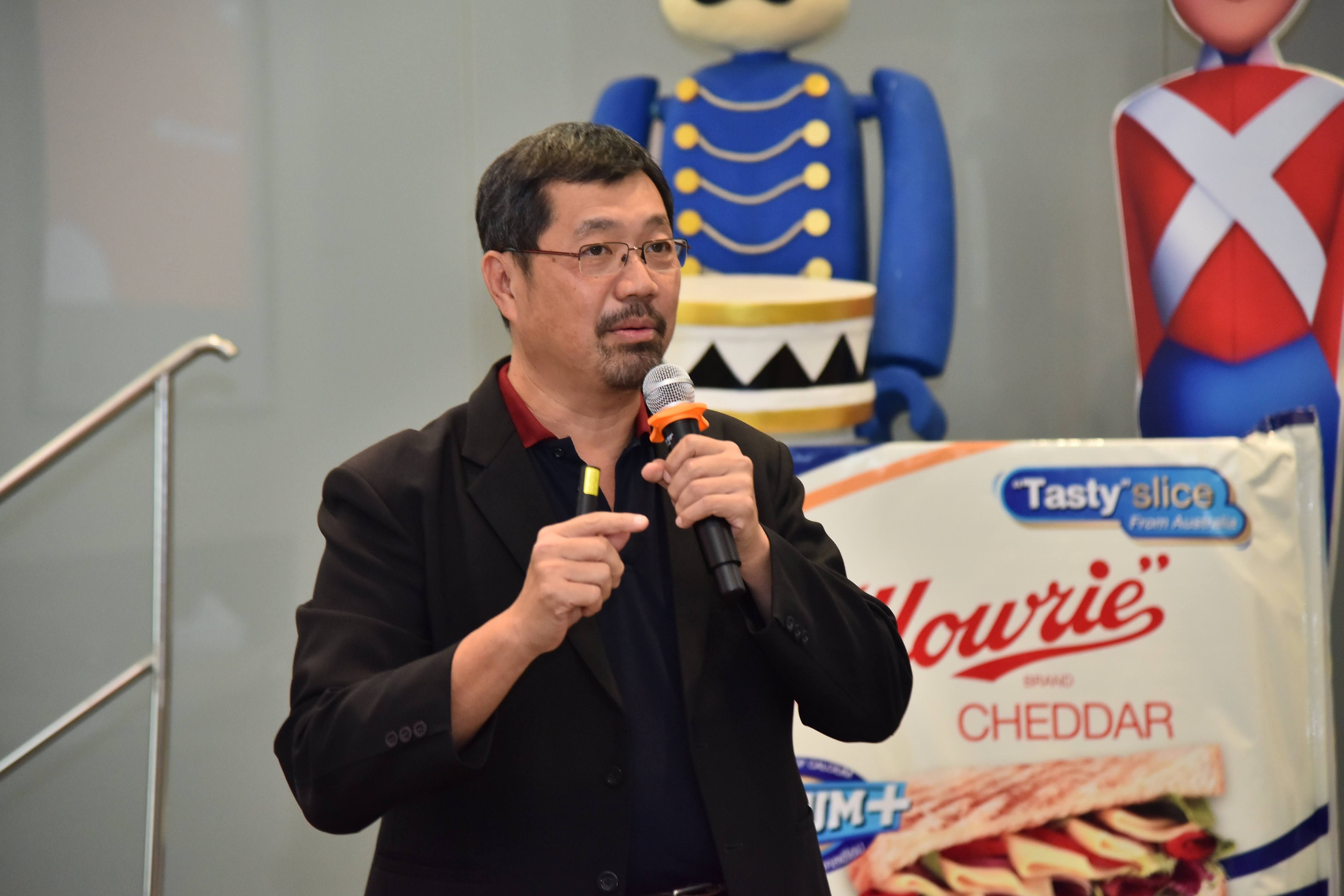 Man with glasses speaking into a microphone, with snack packaging and toy soldiers behind him.