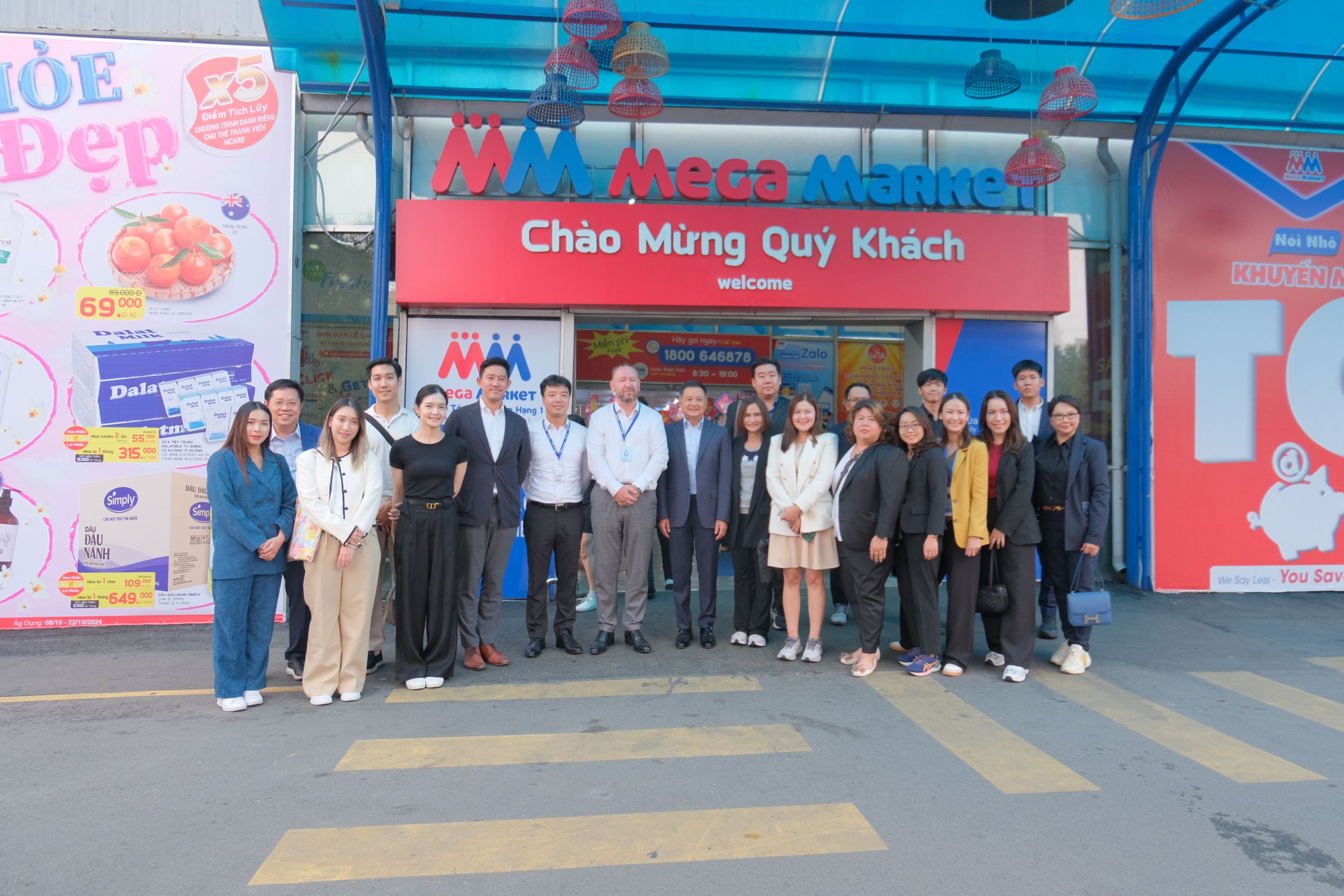 A large group of professionals poses in front of an 'MM Mega Market' store entrance.