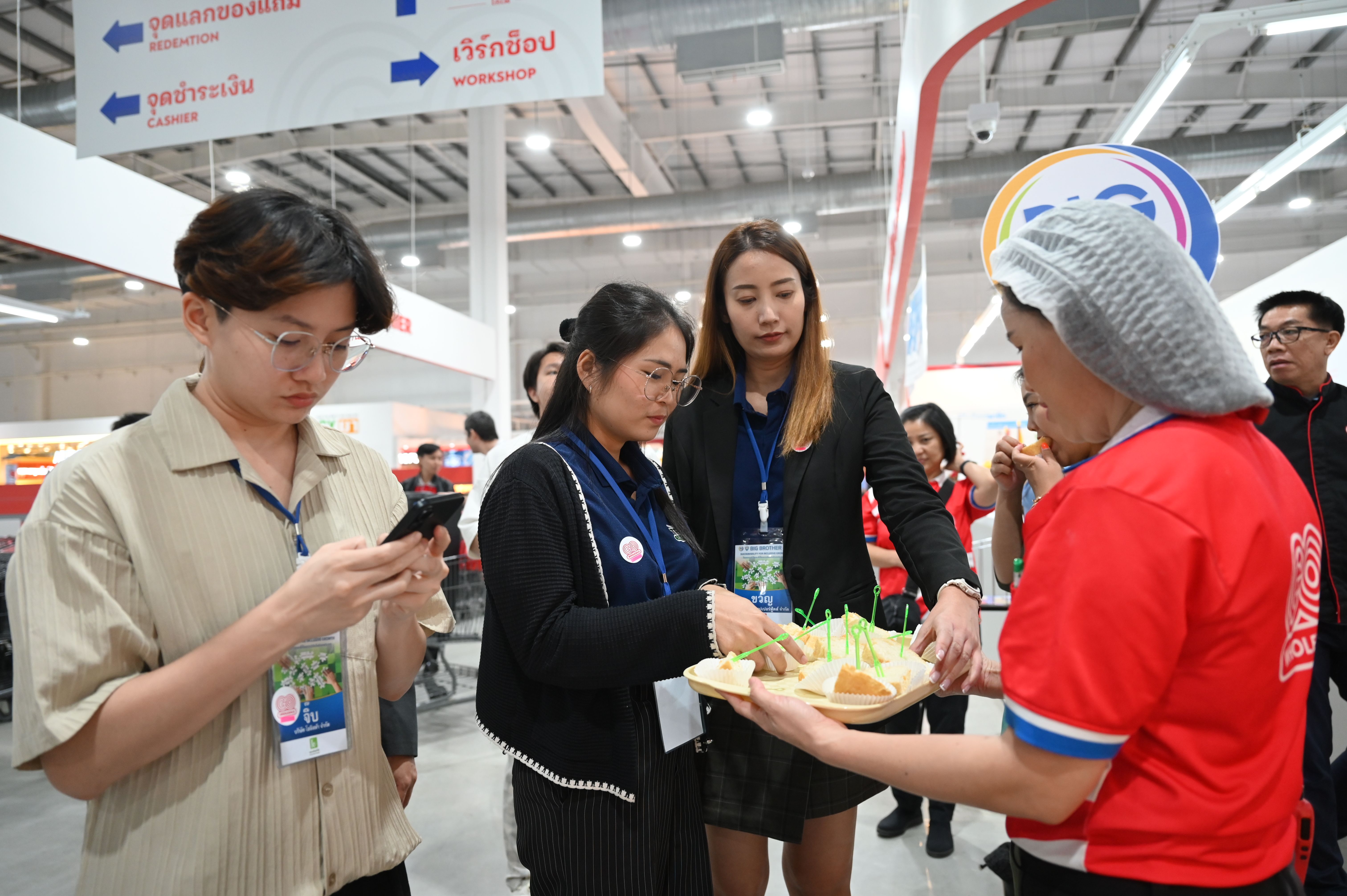 A woman in red serves food samples to two people at an indoor event or store.
