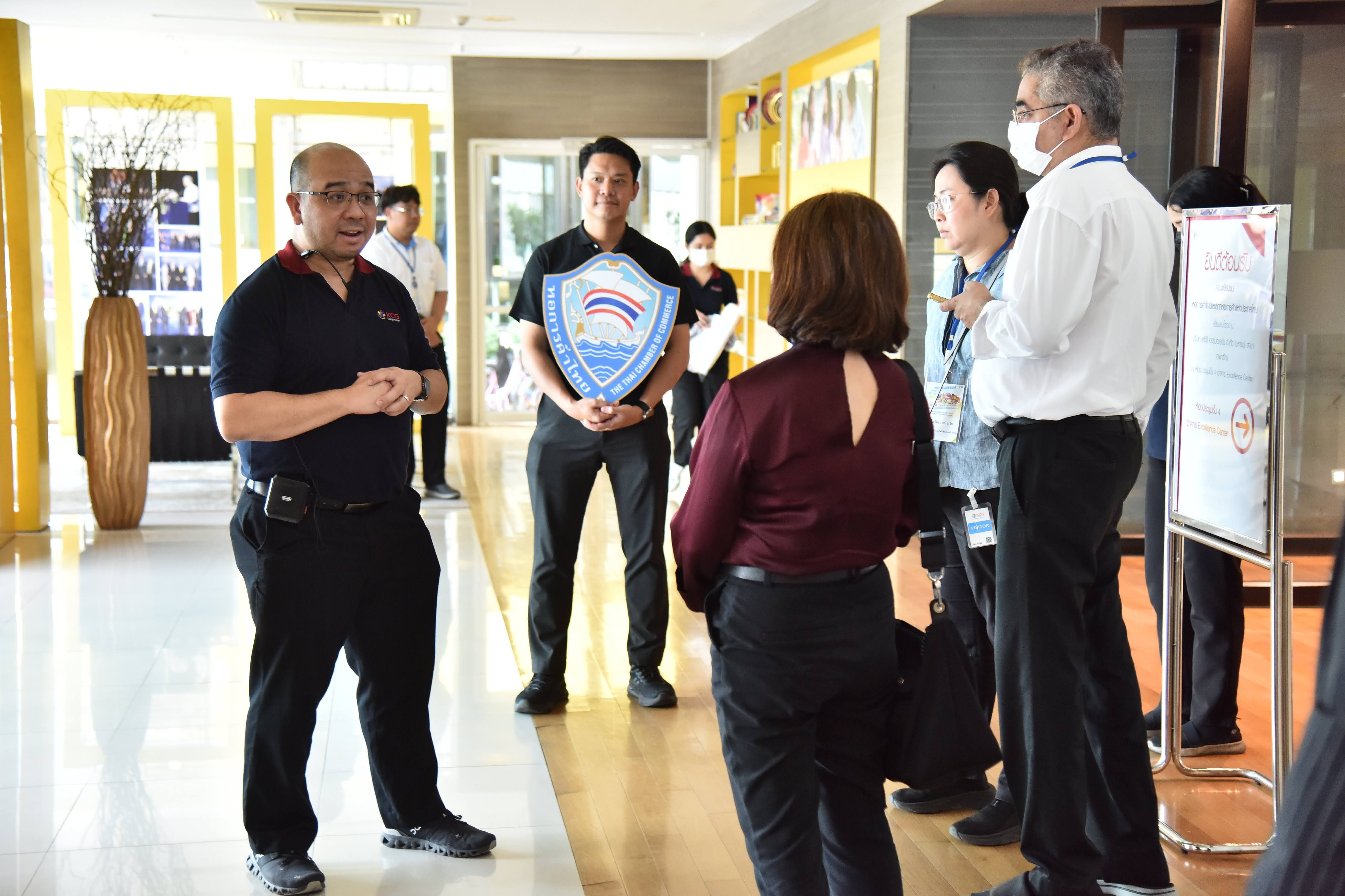 Man in black polo shirt speaks to a group, while another holds a shield award.