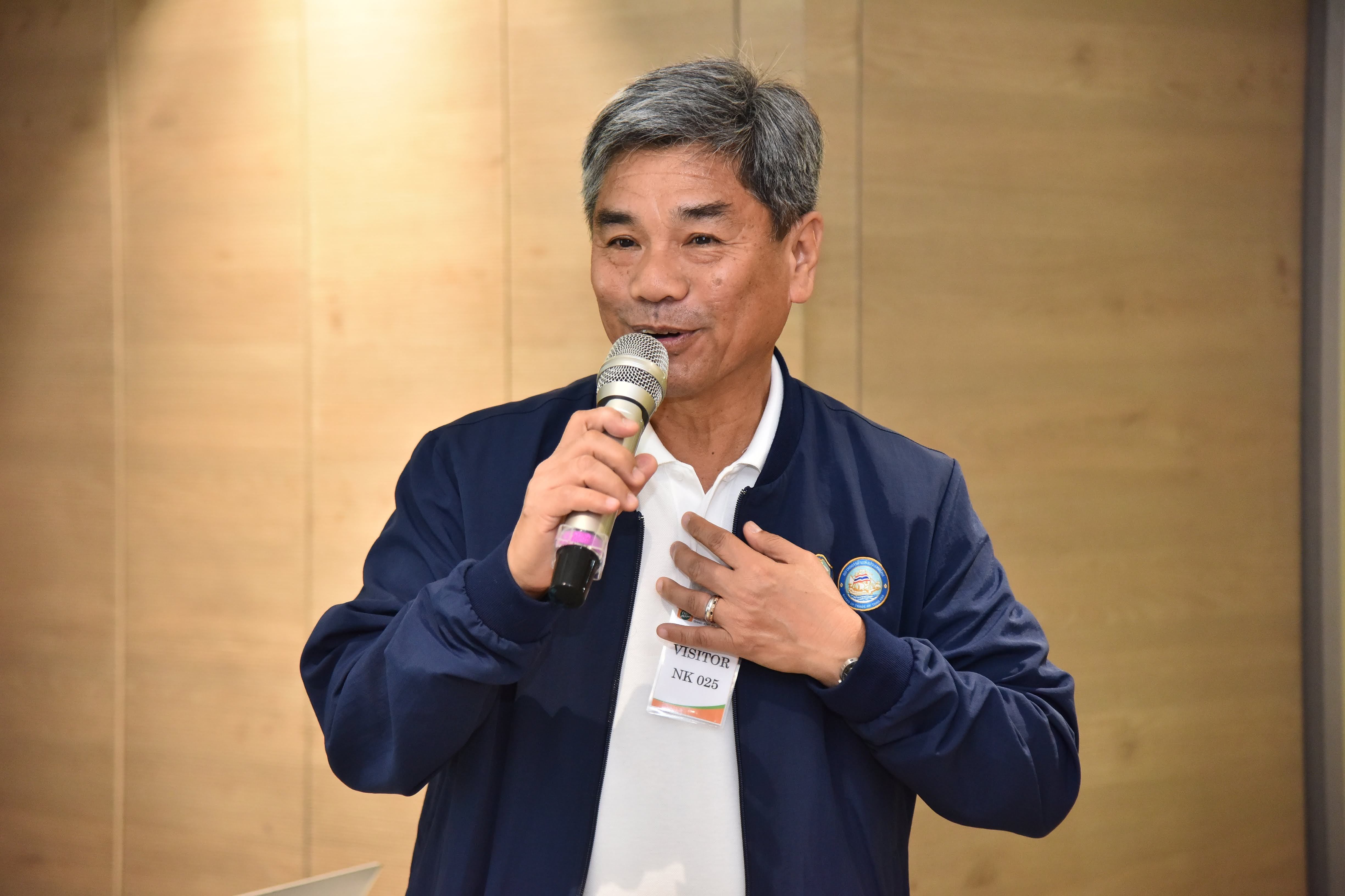 Middle-aged man in a blue jacket speaks into a microphone during a presentation.
