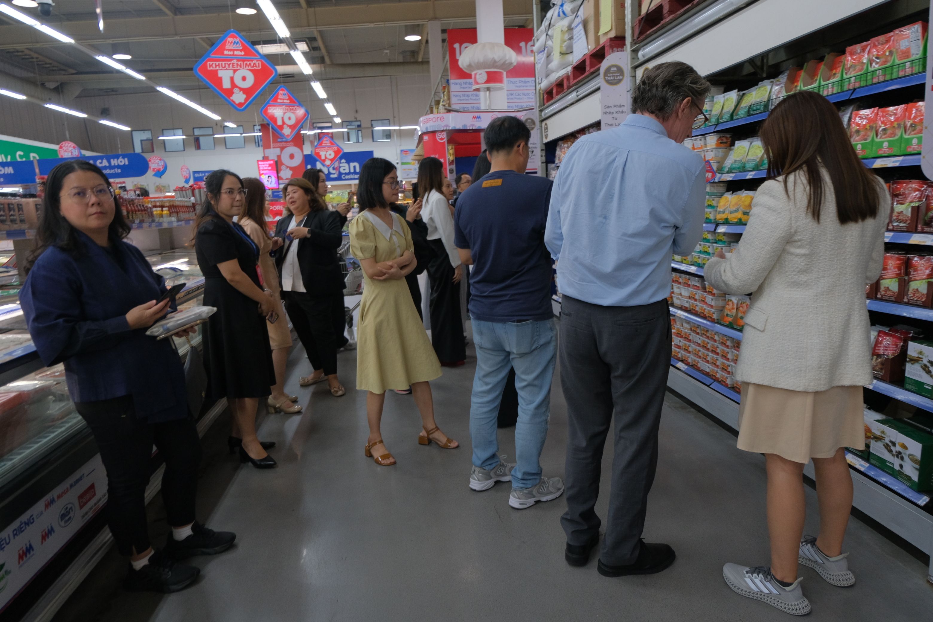 Customers browse products in a brightly lit supermarket aisle with various goods on display.