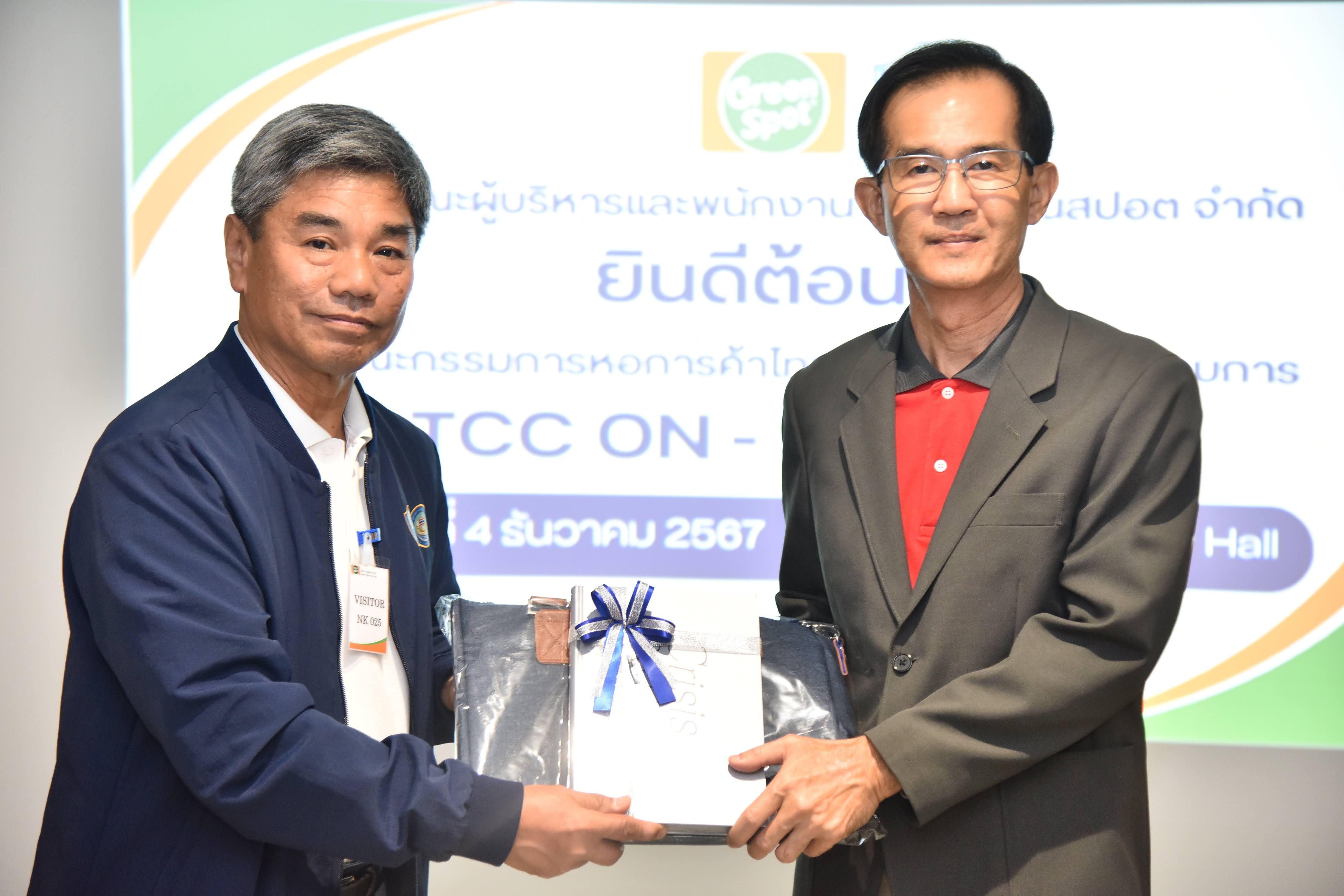 Two men exchange a wrapped gift package during an indoor ceremony.