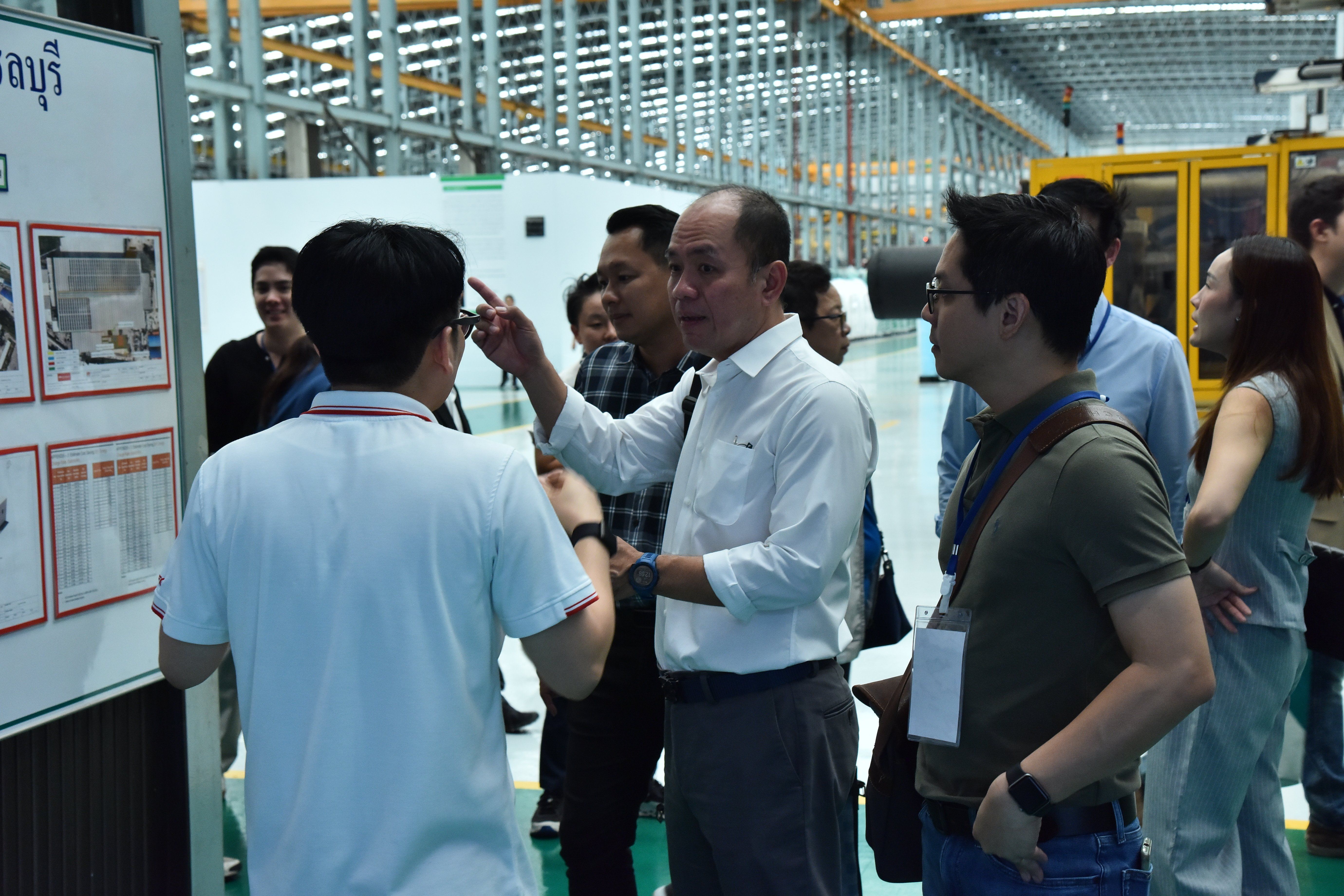 Man in white shirt explains to a group gathered around a factory whiteboard.
