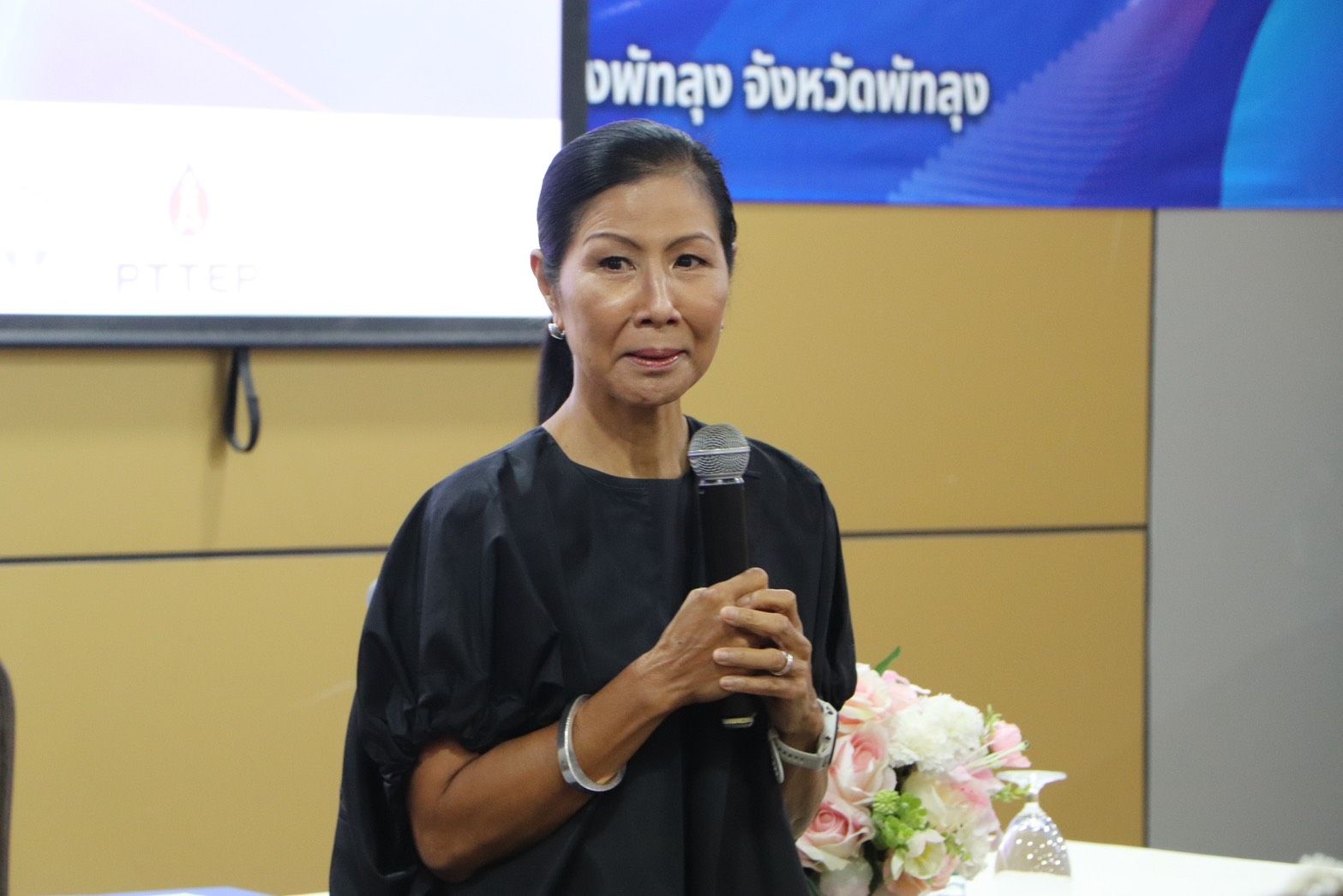 Woman in dark top holding a microphone, speaking at a presentation.