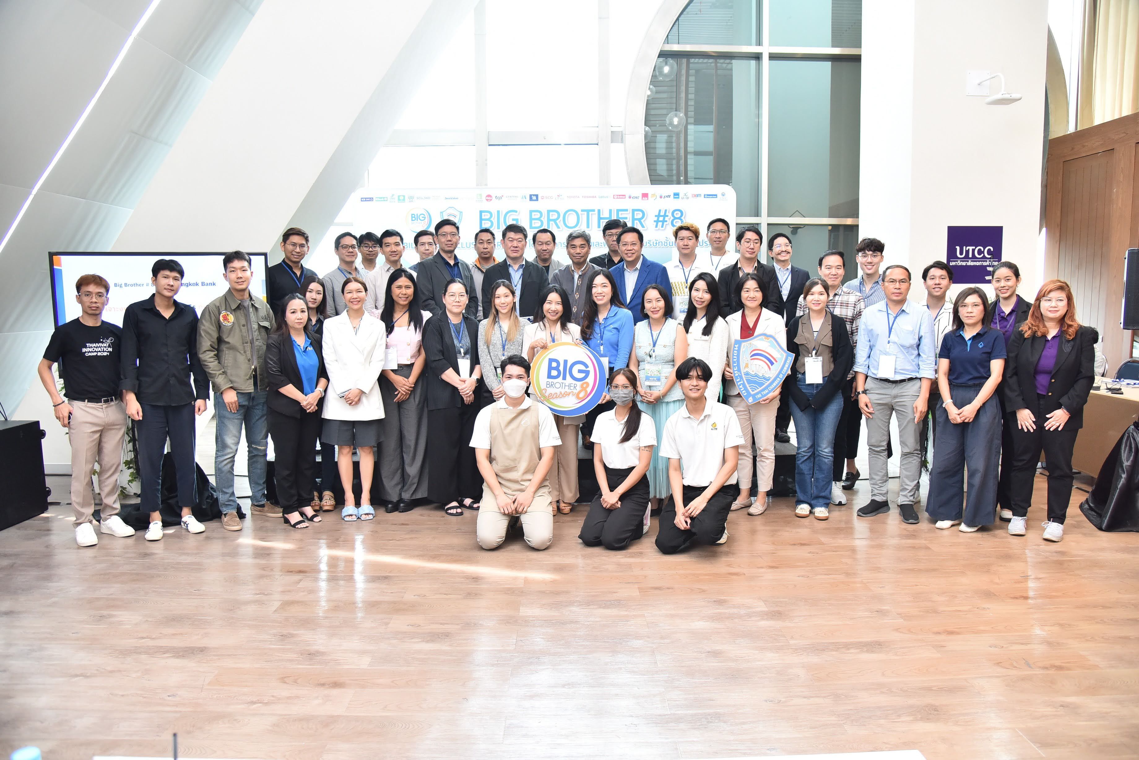A diverse group of professionals poses for a group photo in a bright event hall.