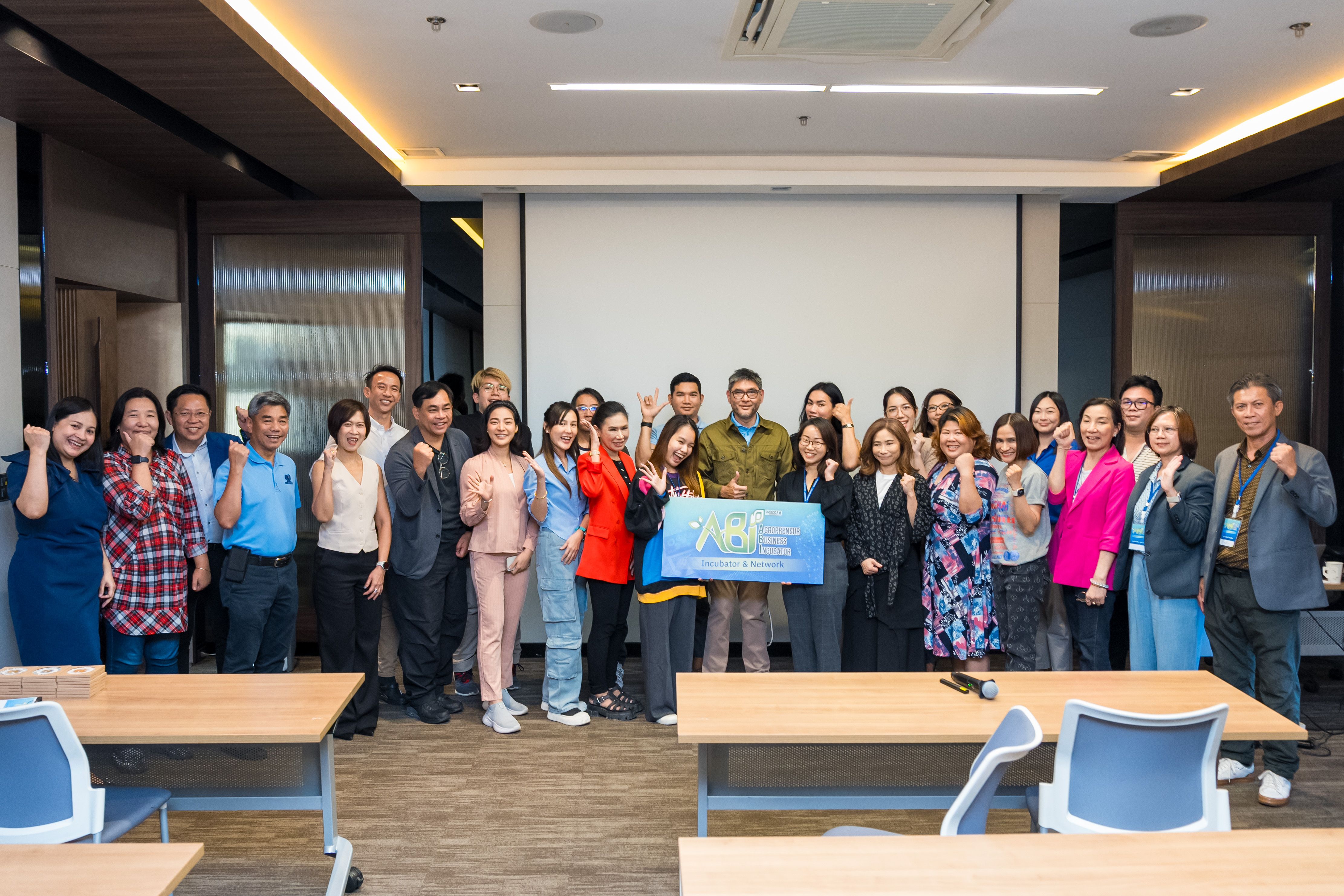 A large group of diverse professionals smiling and raising fists in a modern conference room.