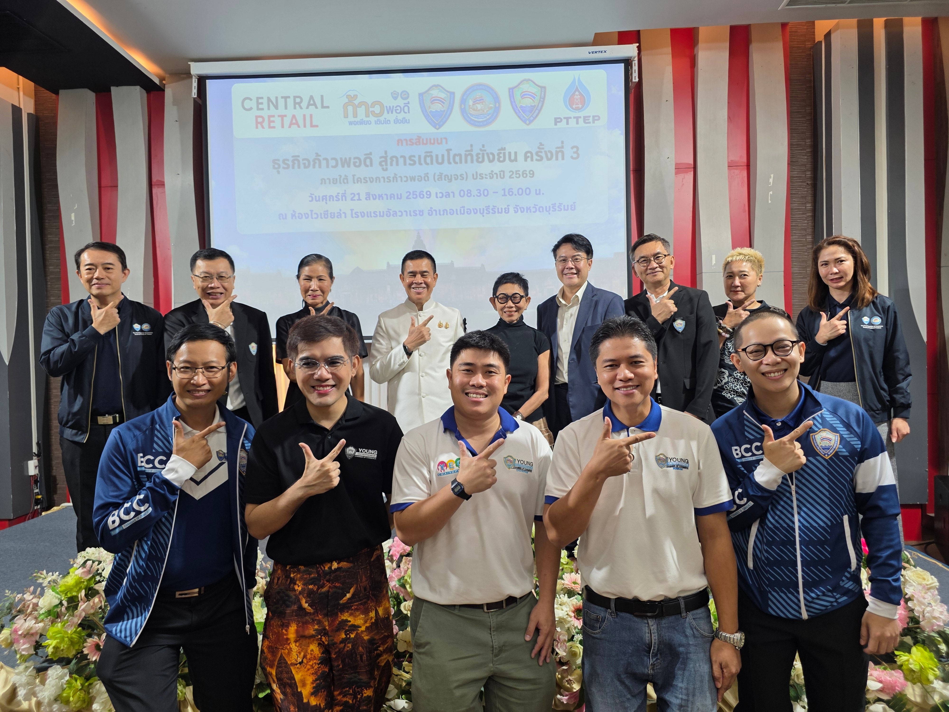 Group of diverse individuals, mostly men, posing with a unified hand gesture in a conference room.