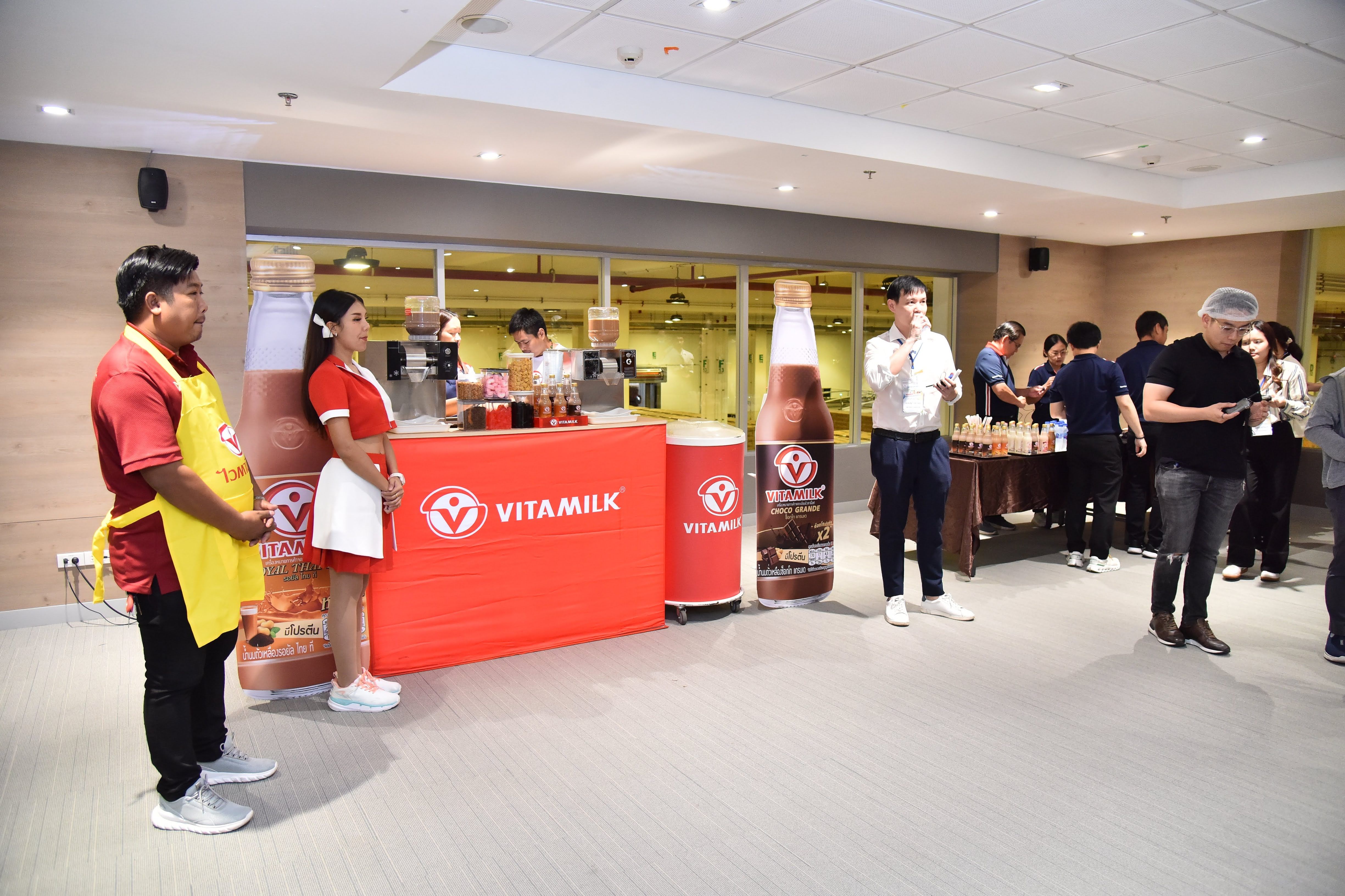 Staff stand by a Vita Milk booth with large product displays at an indoor event.