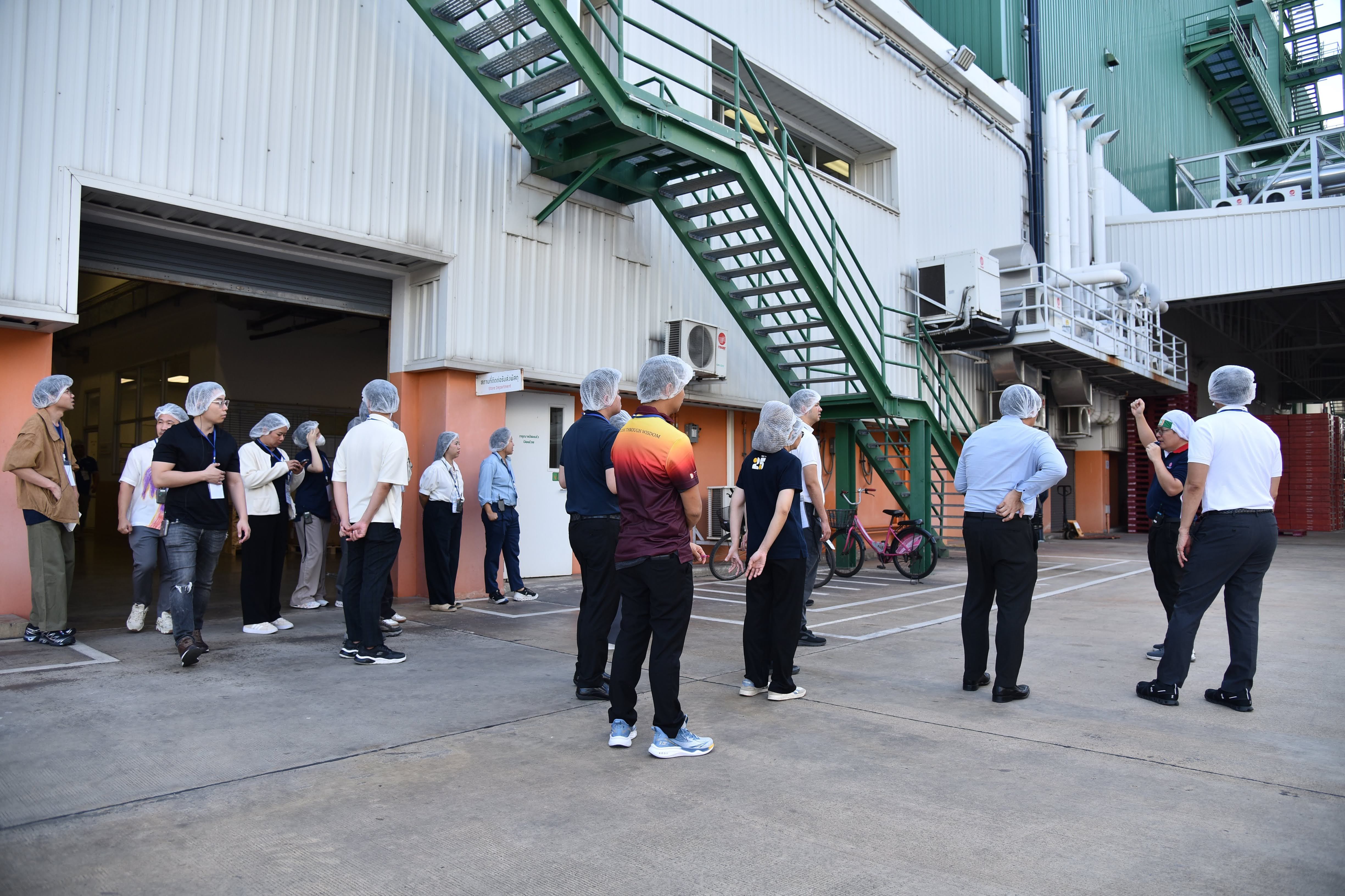 Group of people wearing hairnets touring an industrial facility with a green staircase.