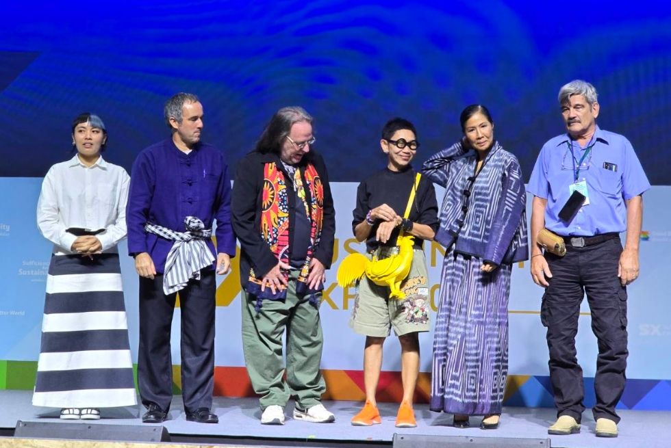 Six diverse people in various traditional and casual attire stand on a stage.