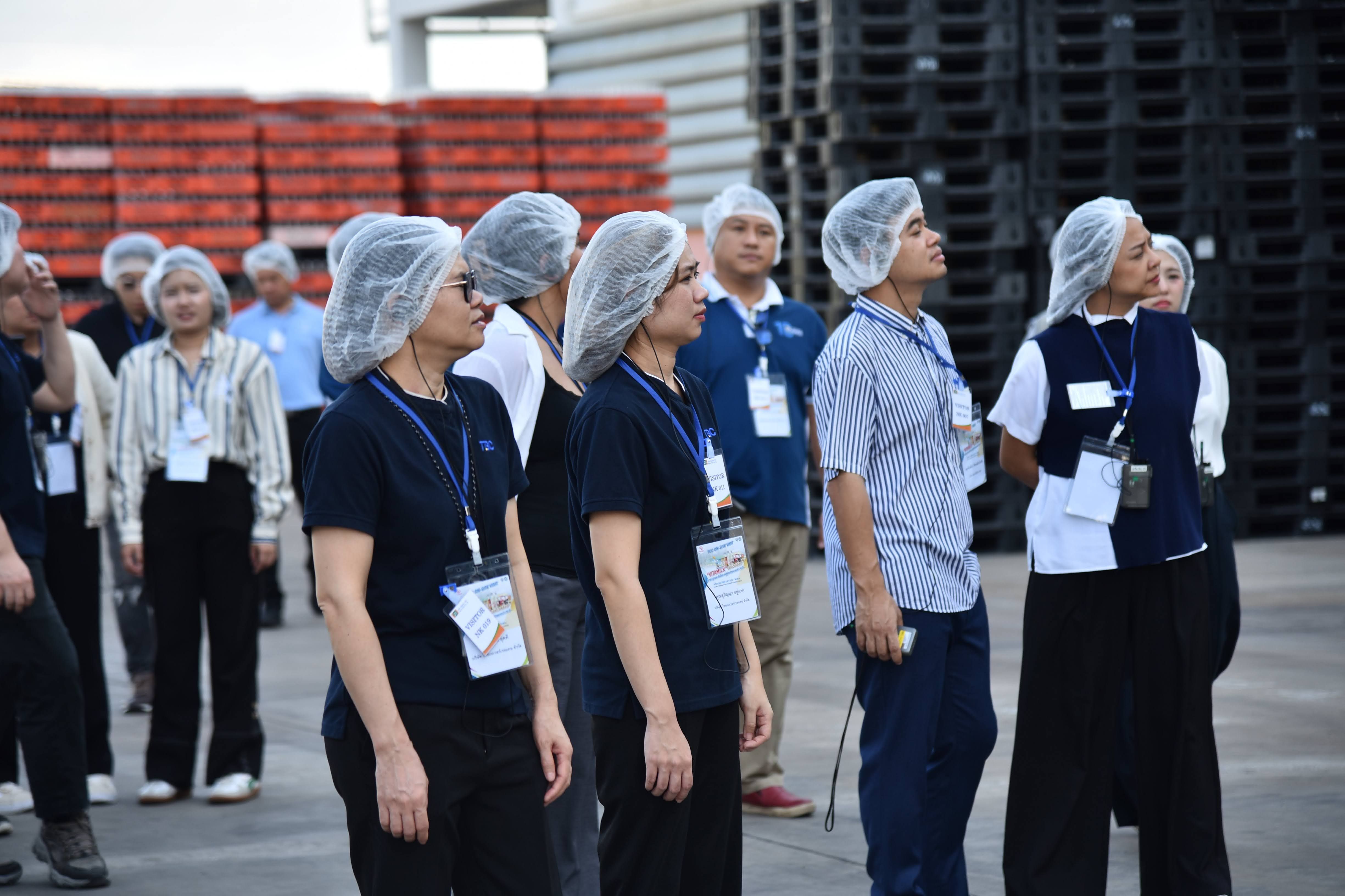 Group of professionals in hairnets observe facility operations during a tour.