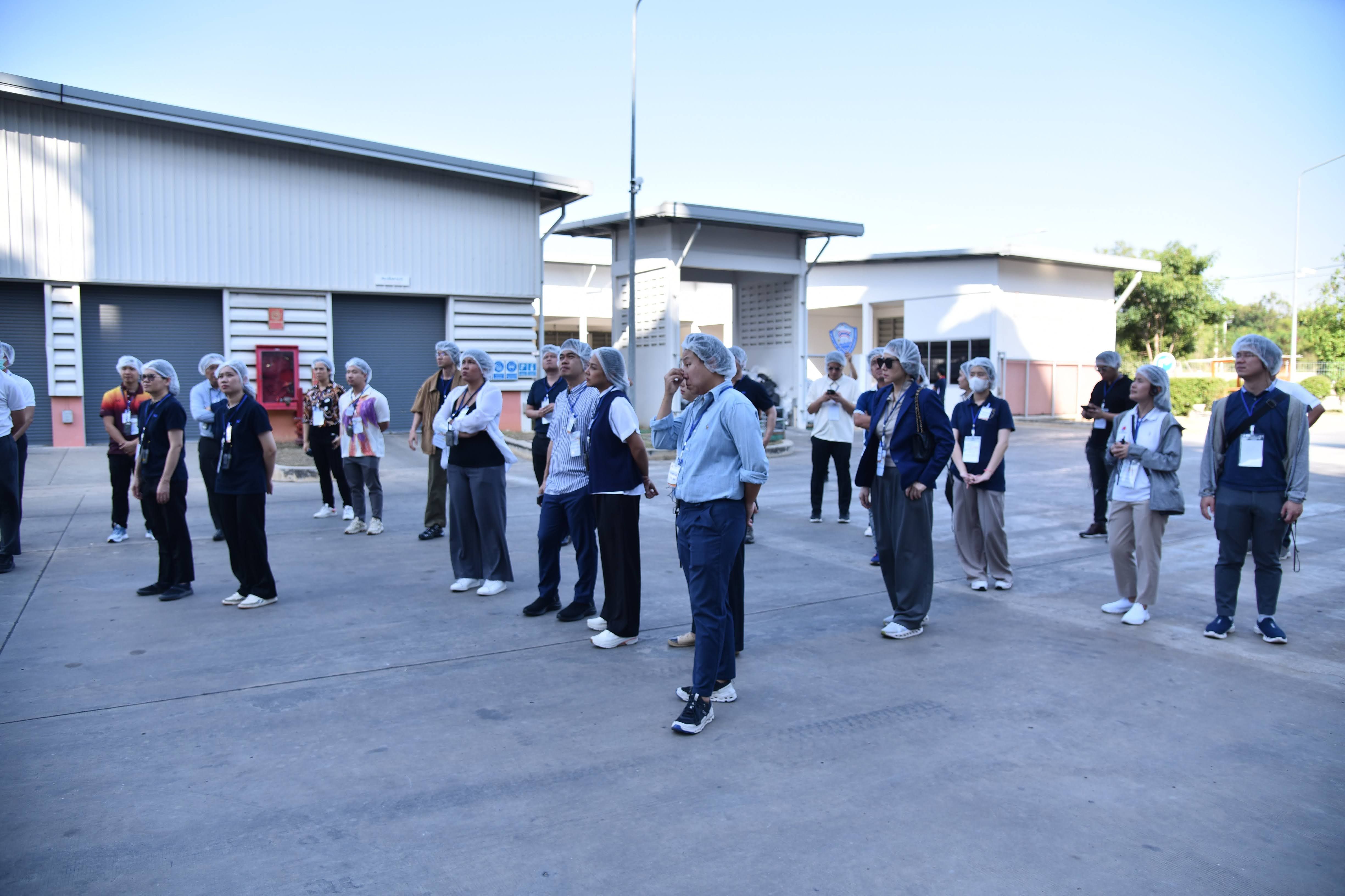 A group of older adults stands outside industrial buildings, looking attentively.