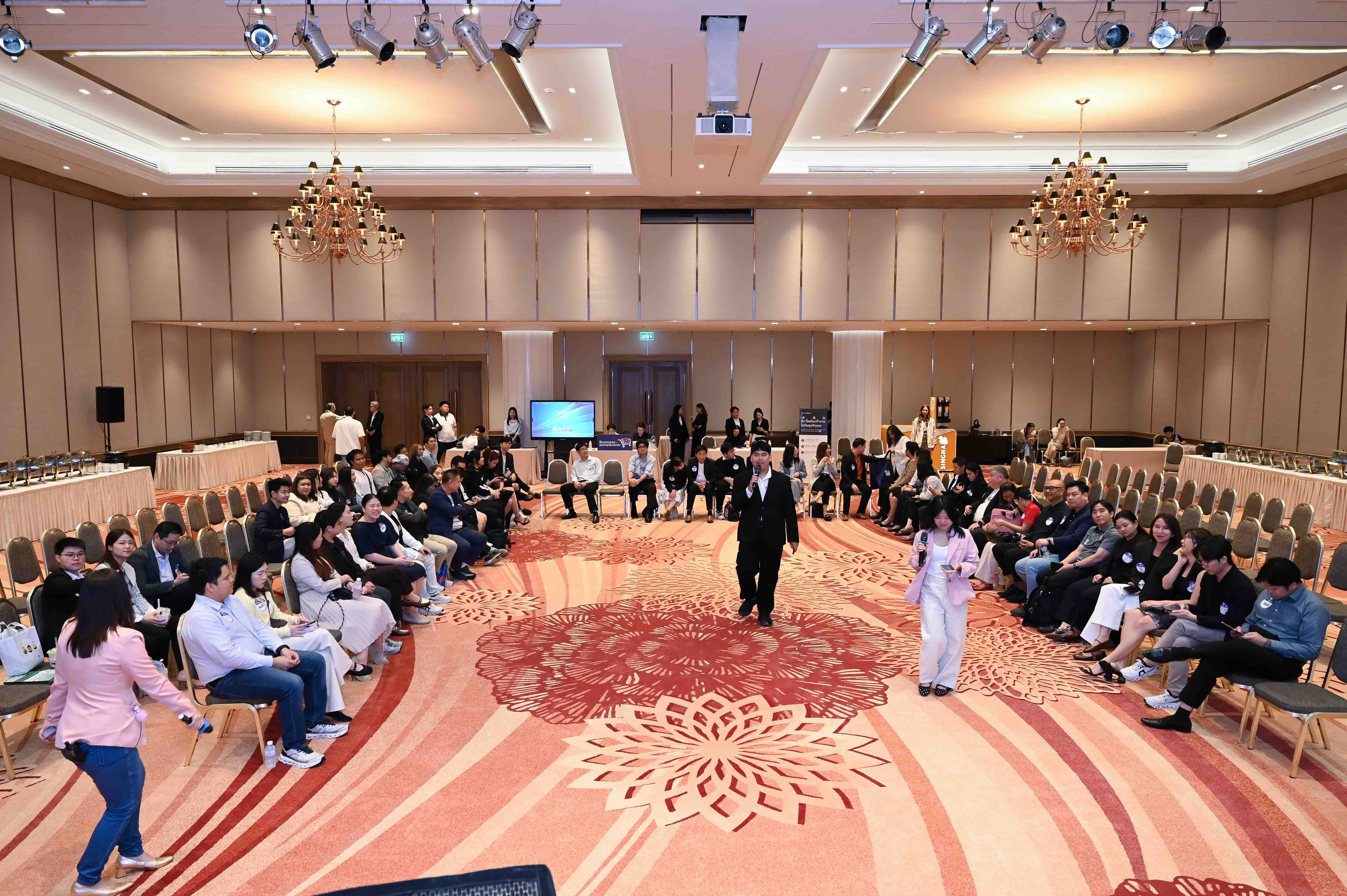 Attendees sit in a large conference room listening to a presenter at a circular meeting.