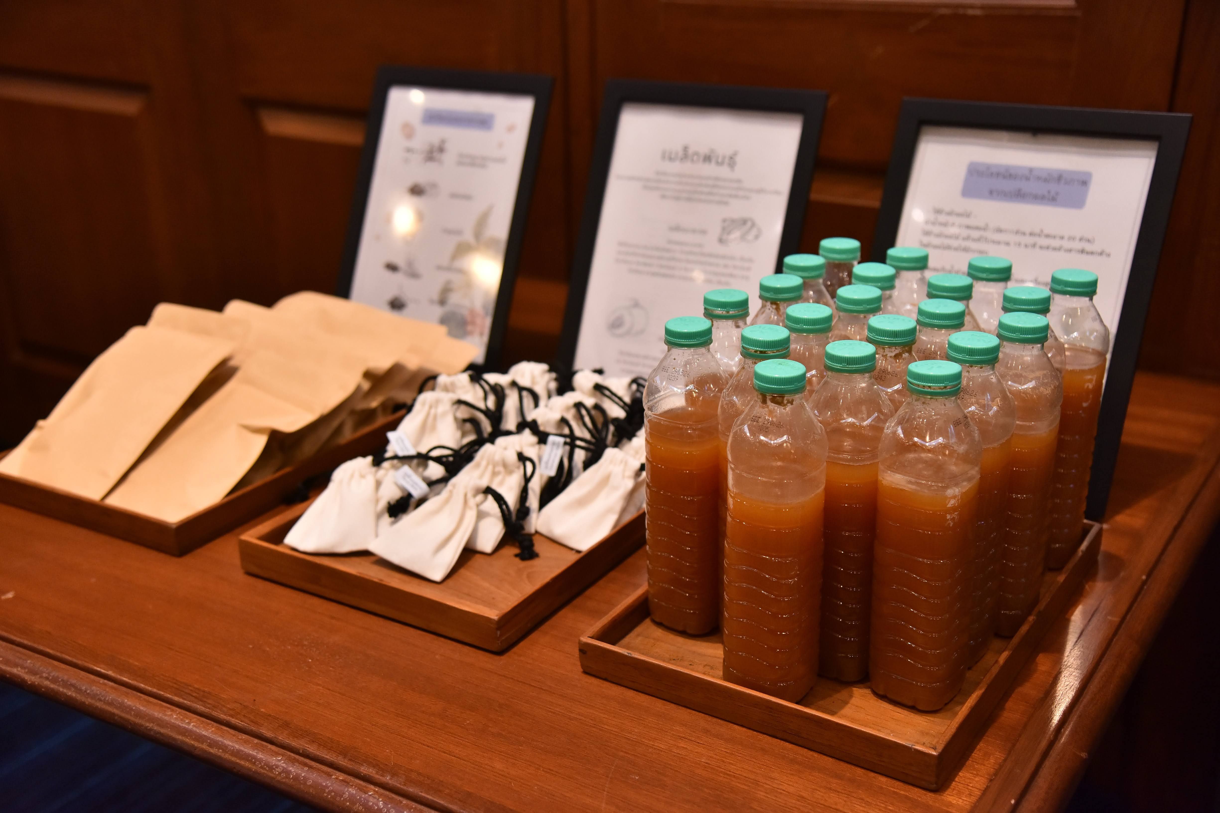 Three trays display brown bags, wrapped snacks, and bottled brown beverages with green caps.